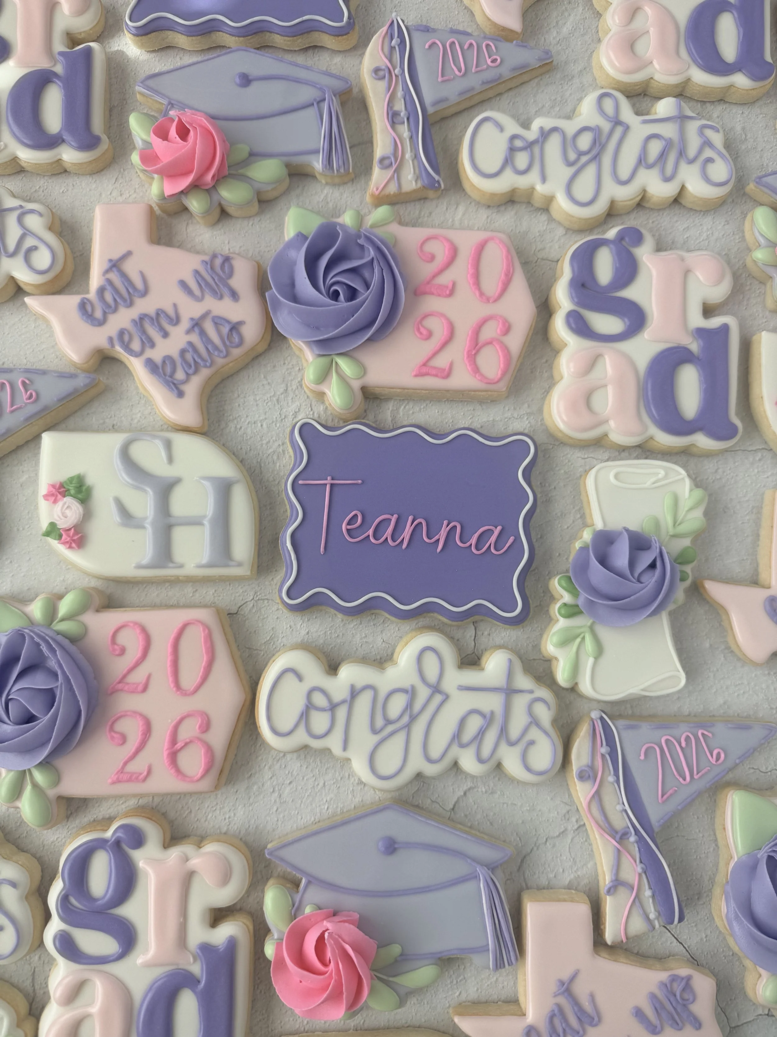 Decorated cookies with graduation and celebration themes in pastel colors, including messages like "Congrats," "eat them up Kate," and "Tears" with the date 2026, along with graduation caps and roses.
