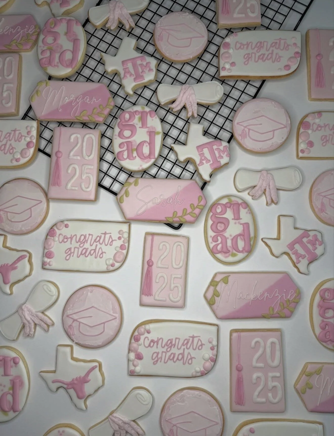 Decorative cookies celebrating graduation and 25th birthday, in pink and white with graduation caps, diplomas, the Texas state outline, the words 'congrats grads', and the year 2025.