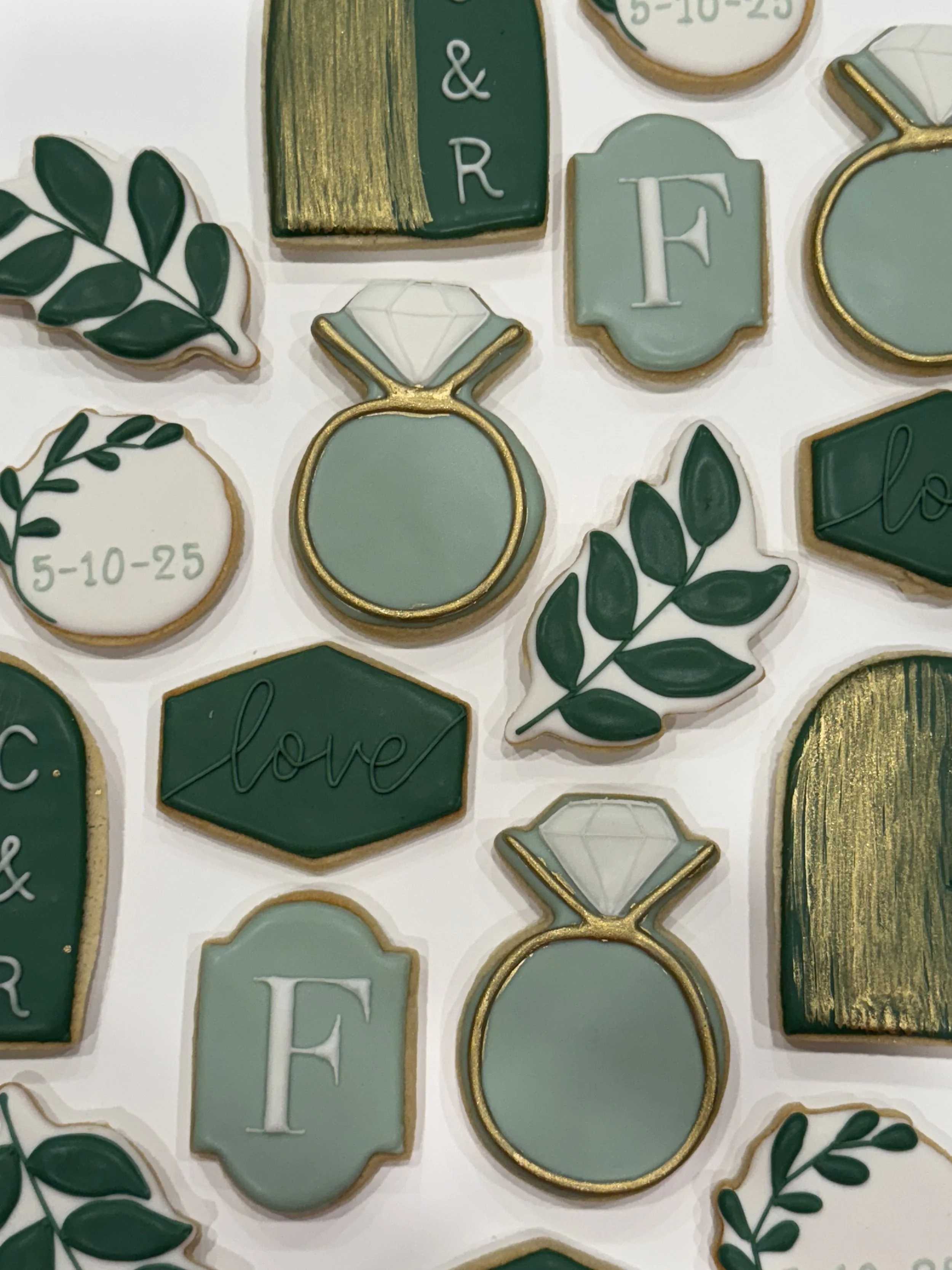 A collection of decorative cookies in green, gold, and white colors featuring various designs including leaves, diamonds, and the word 'love'.