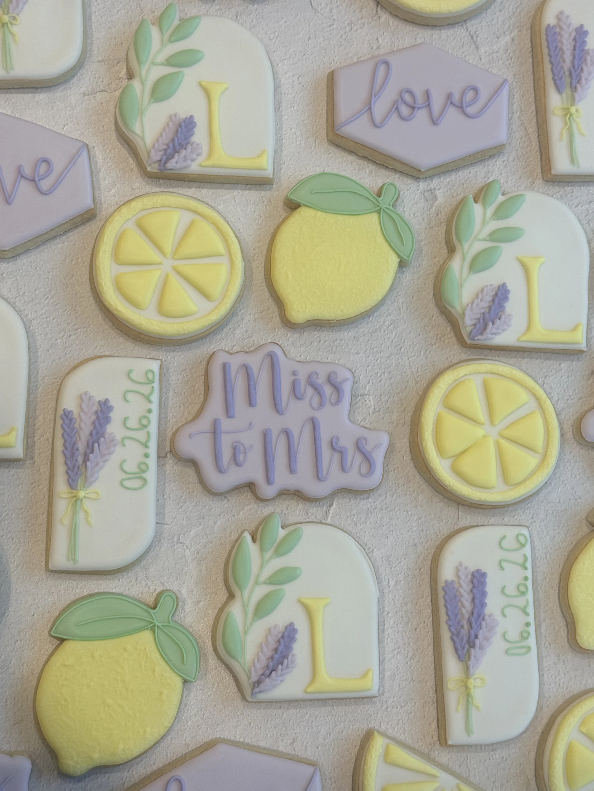 Collection of decorated sugar cookies with lemon, love, and lavender themes, featuring lemons, lemon slices, and lavender sprigs in pastel colors.