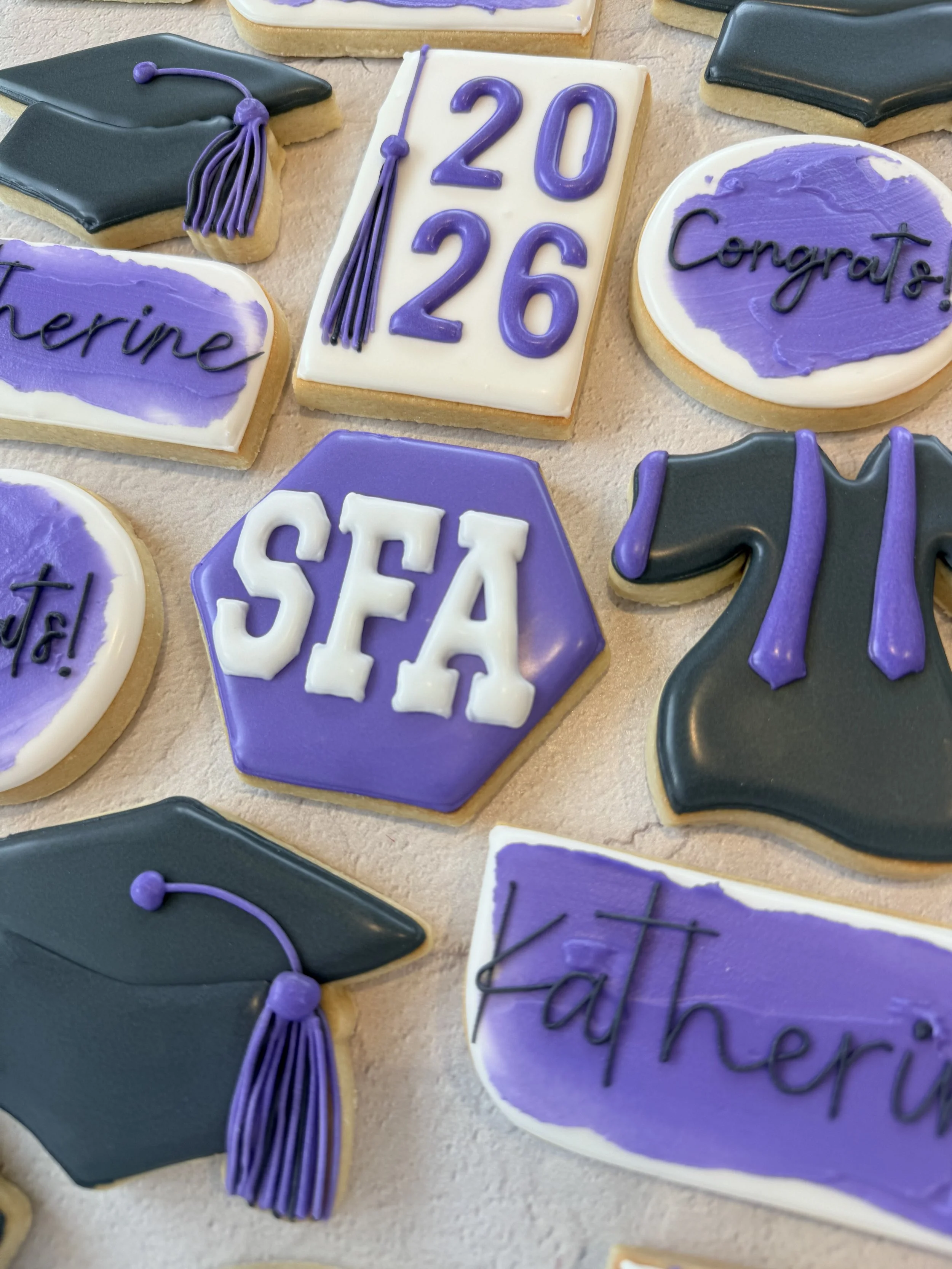 Decorated cookies celebrating a graduation, featuring a diploma with the dates 2020-2026, a graduation cap, and cookies with the names 'Catherine' and 'Conaert'.
