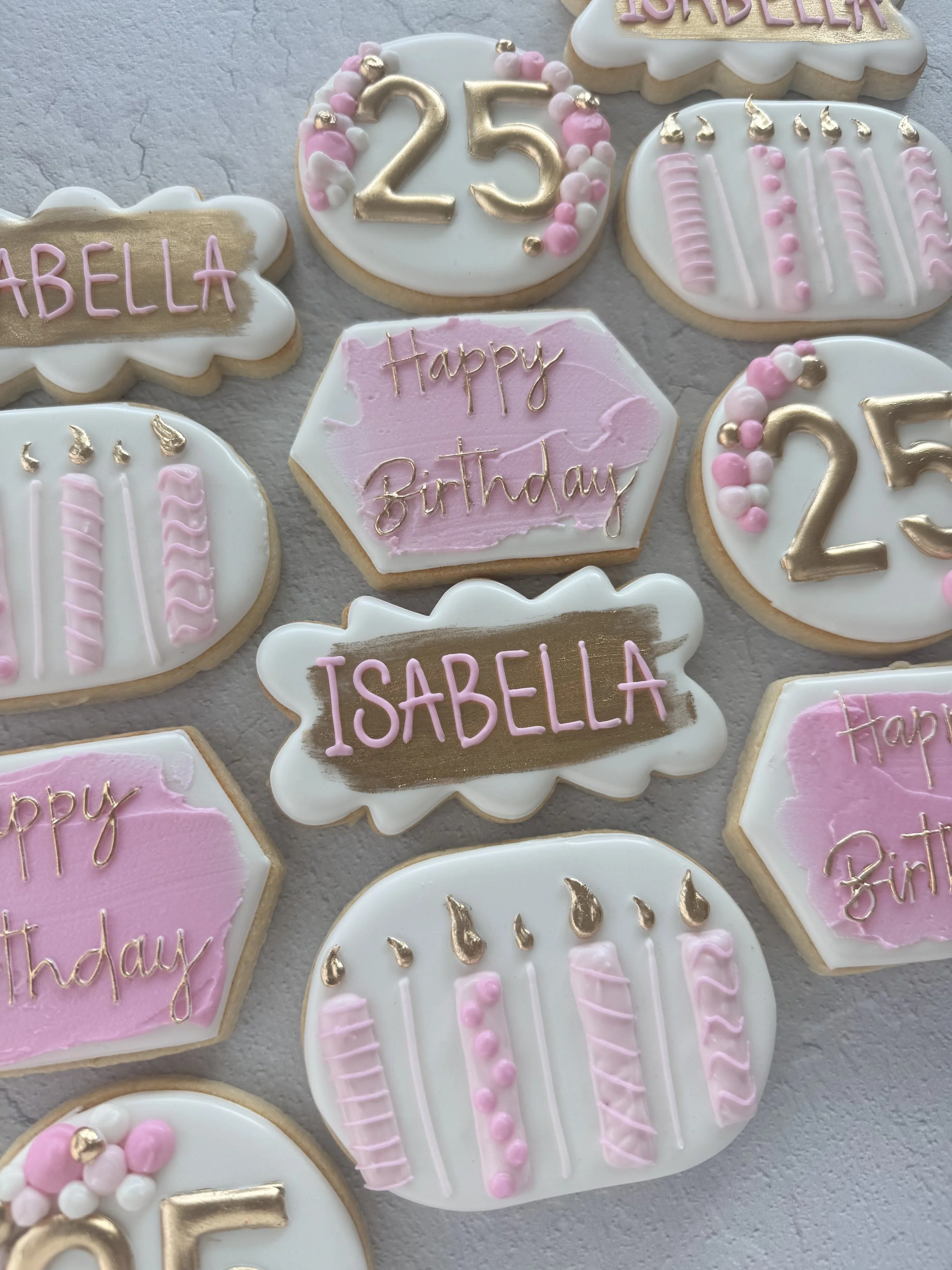 Decorative birthday cookies with pink, white, and gold accents, featuring messages like "Happy Birthday" and "Isabella", and number cookies "25" and "25".