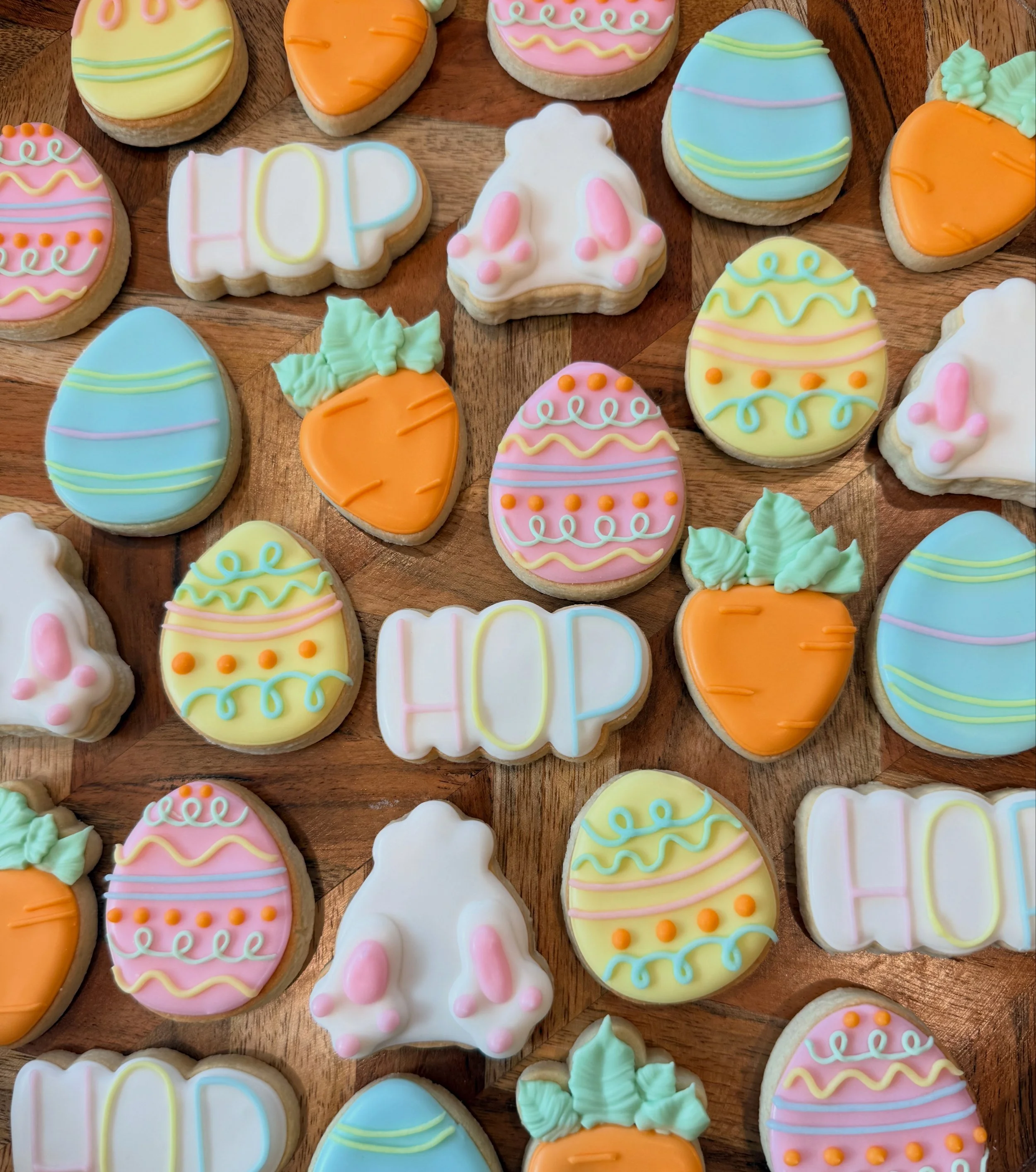 Colorful Easter cookies decorated with pastel icing in various shapes including eggs, carrots, and bunnies, arranged on a wooden surface.