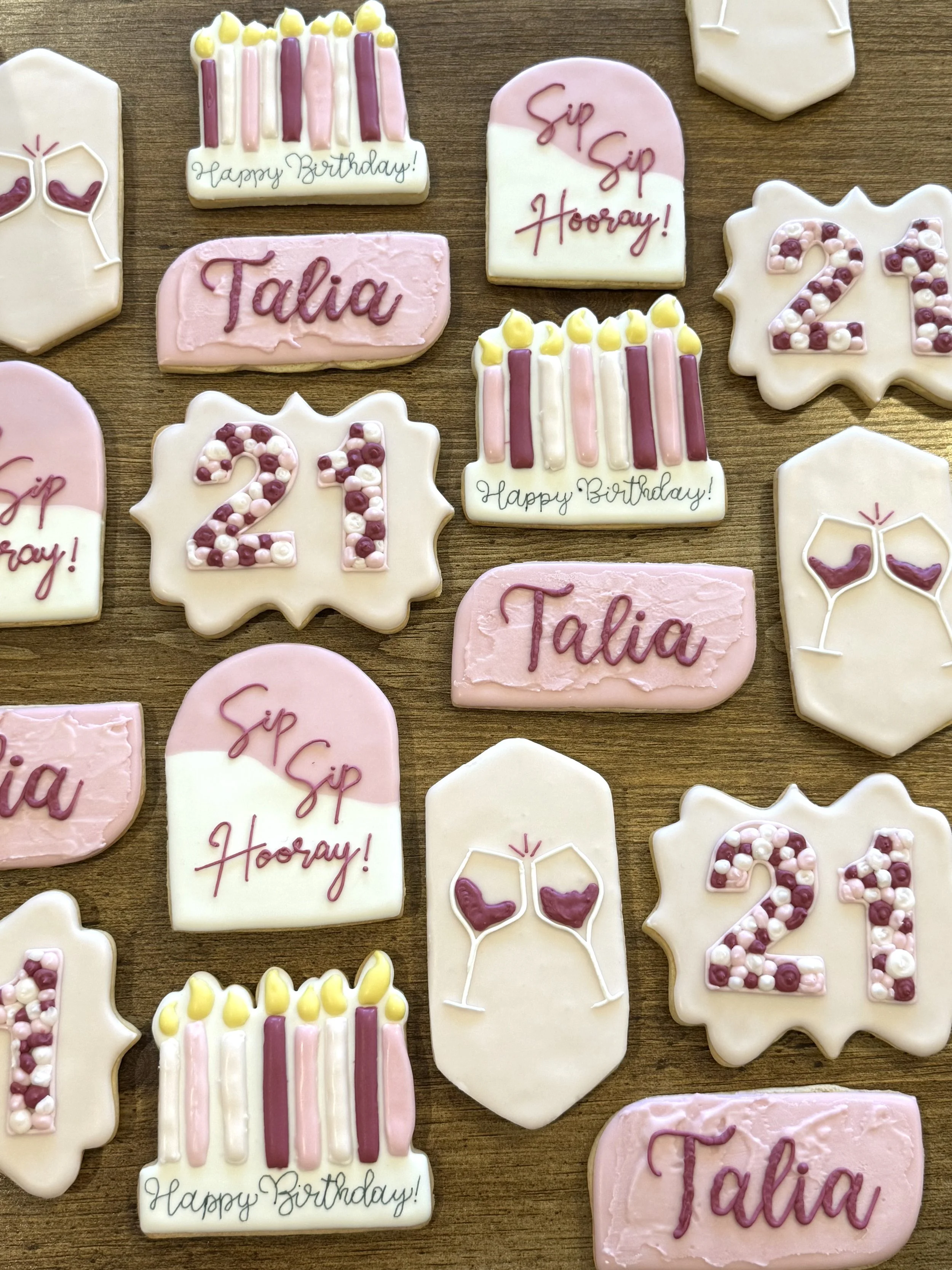 Assorted decorated cookies for a birthday celebration, featuring candles, the number 21, champagne glasses, and birthday messages.