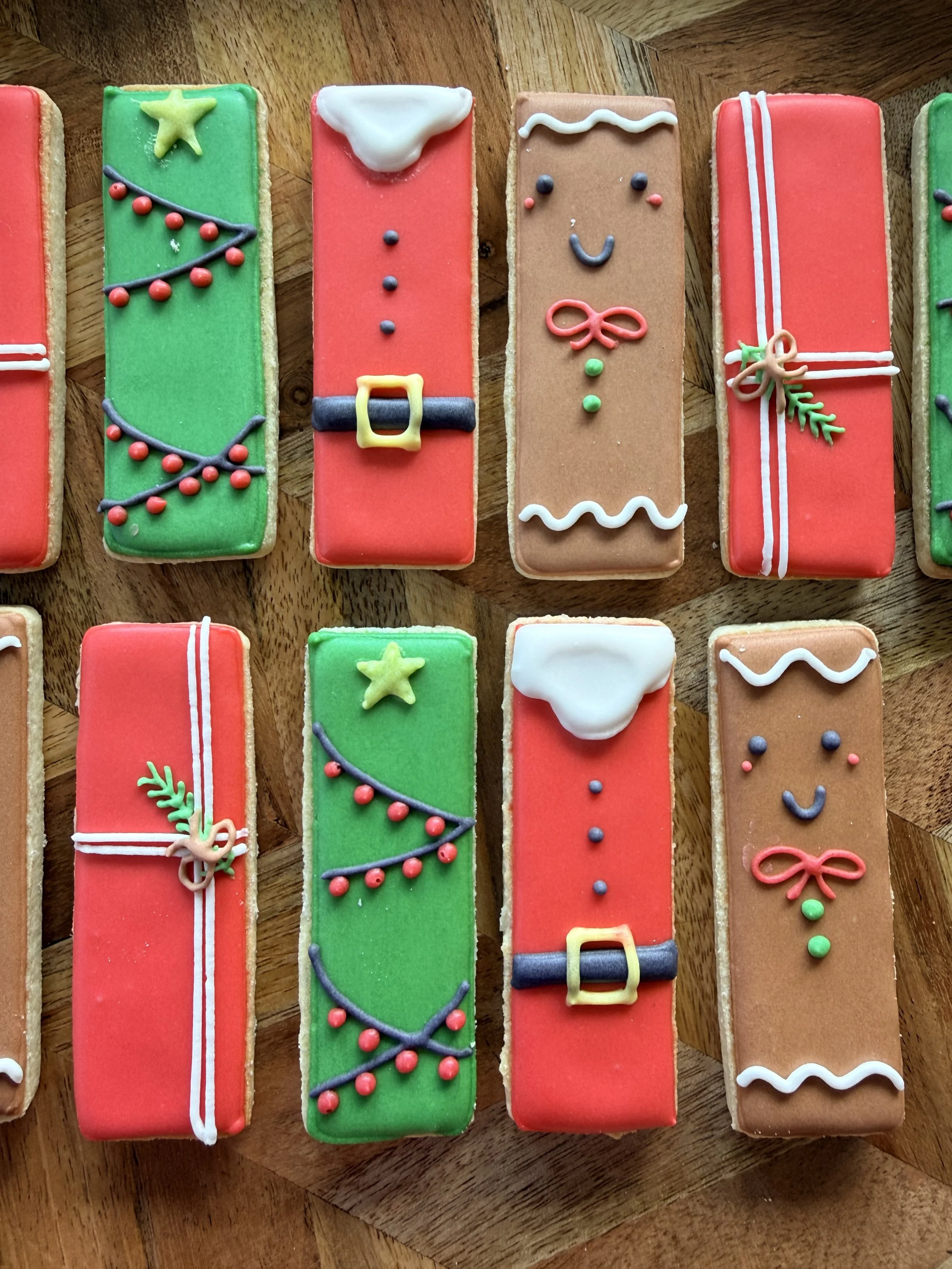 Decorated Christmas-themed cookies shaped like presents with colorful icing, bows, holly, and festive icing decorations, arranged on a wooden surface.