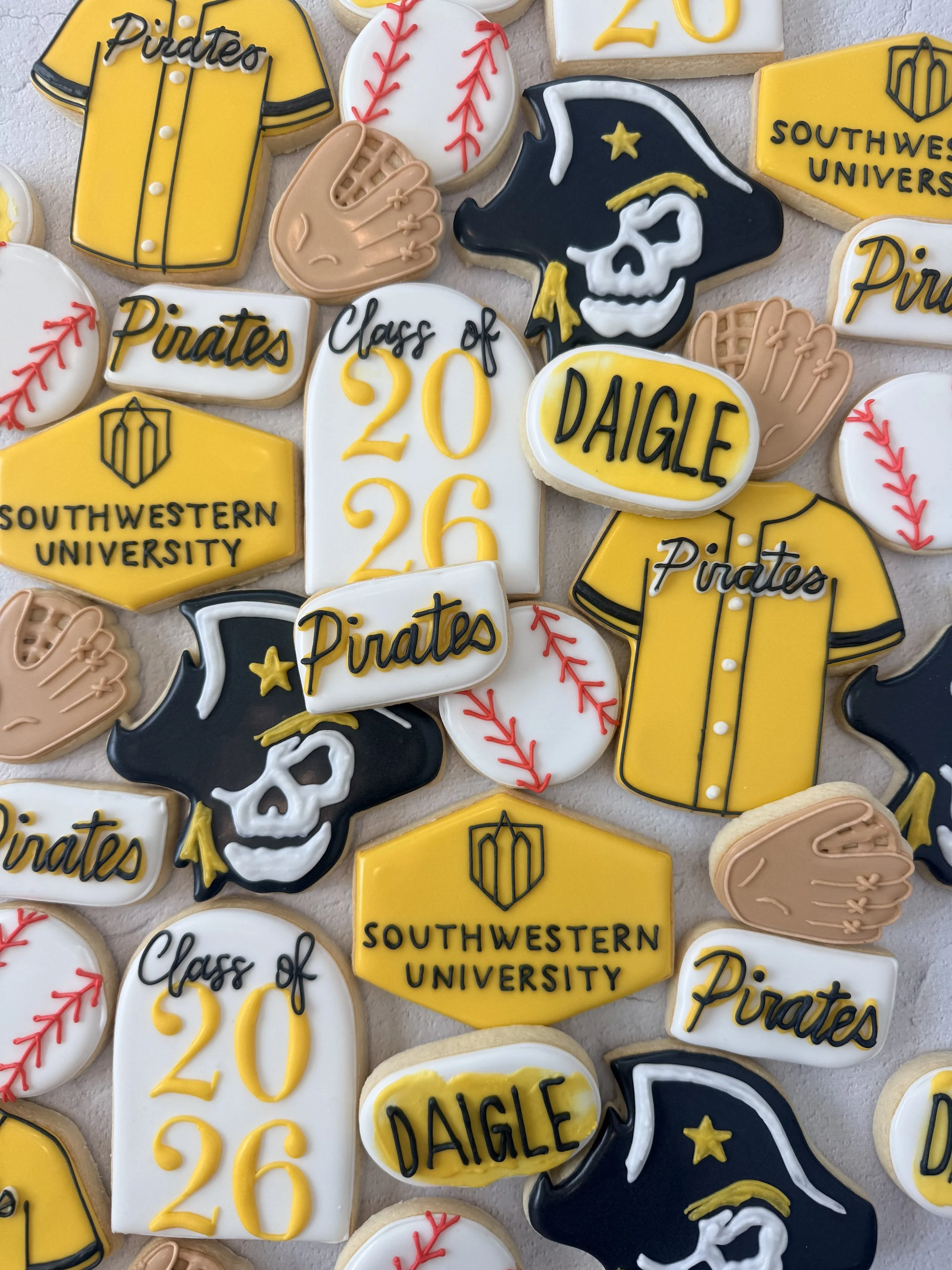Decorated cookies with baseball, pirate, and university logos, featuring yellow, black, white, red, and tan colors.