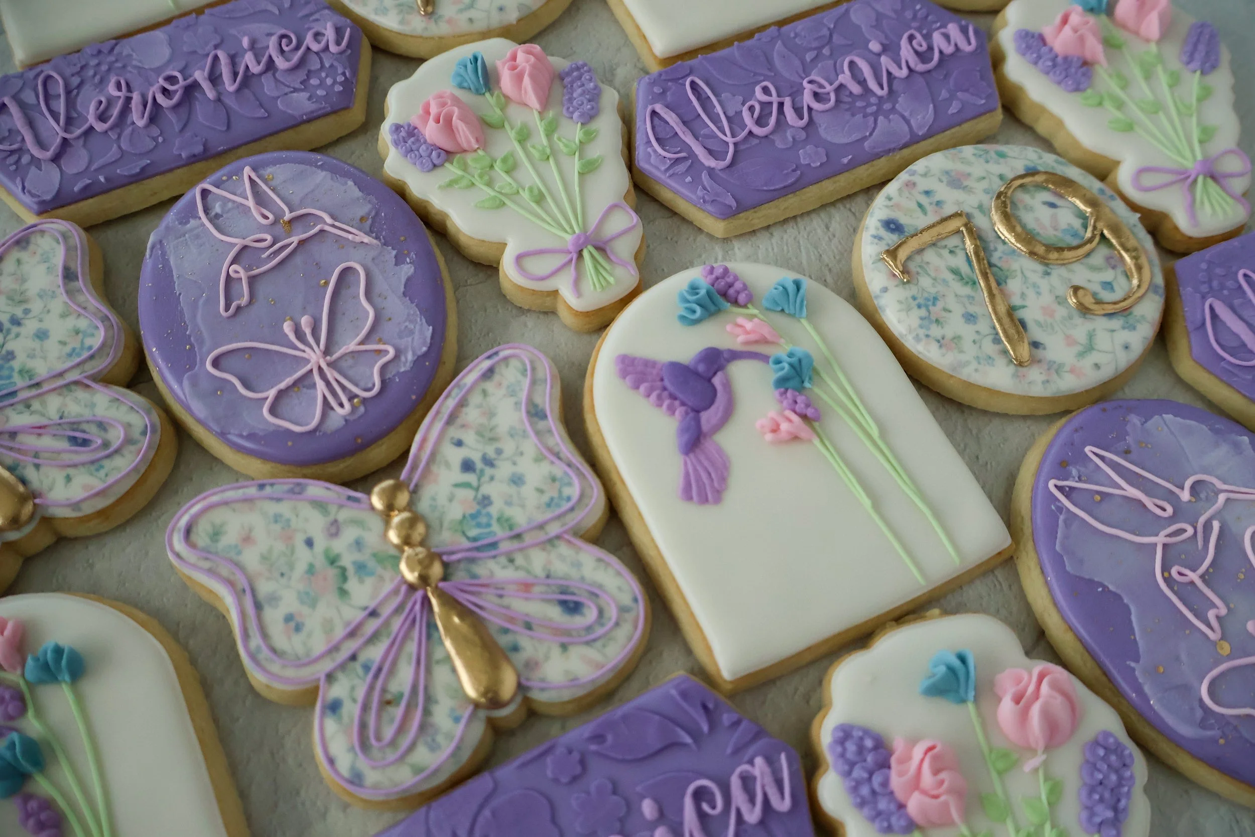 Decorated cookies with lavender and pink frosting, some with flowers, butterflies, and the names Veronica and Alyson, and a number 13.