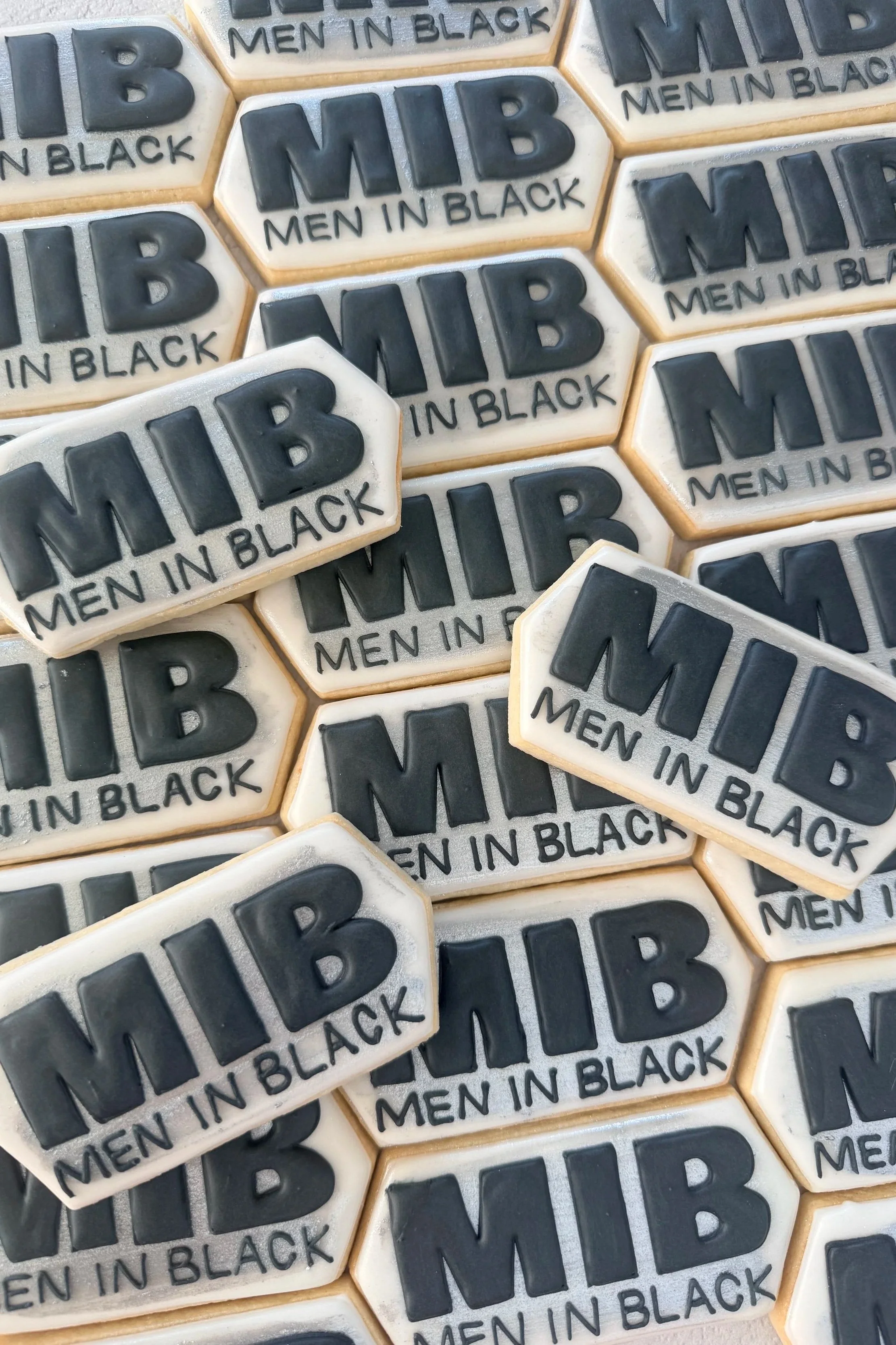 Close-up of hexagonal cookies with black and white icing, displaying the text "MIB MEN IN BLACK".