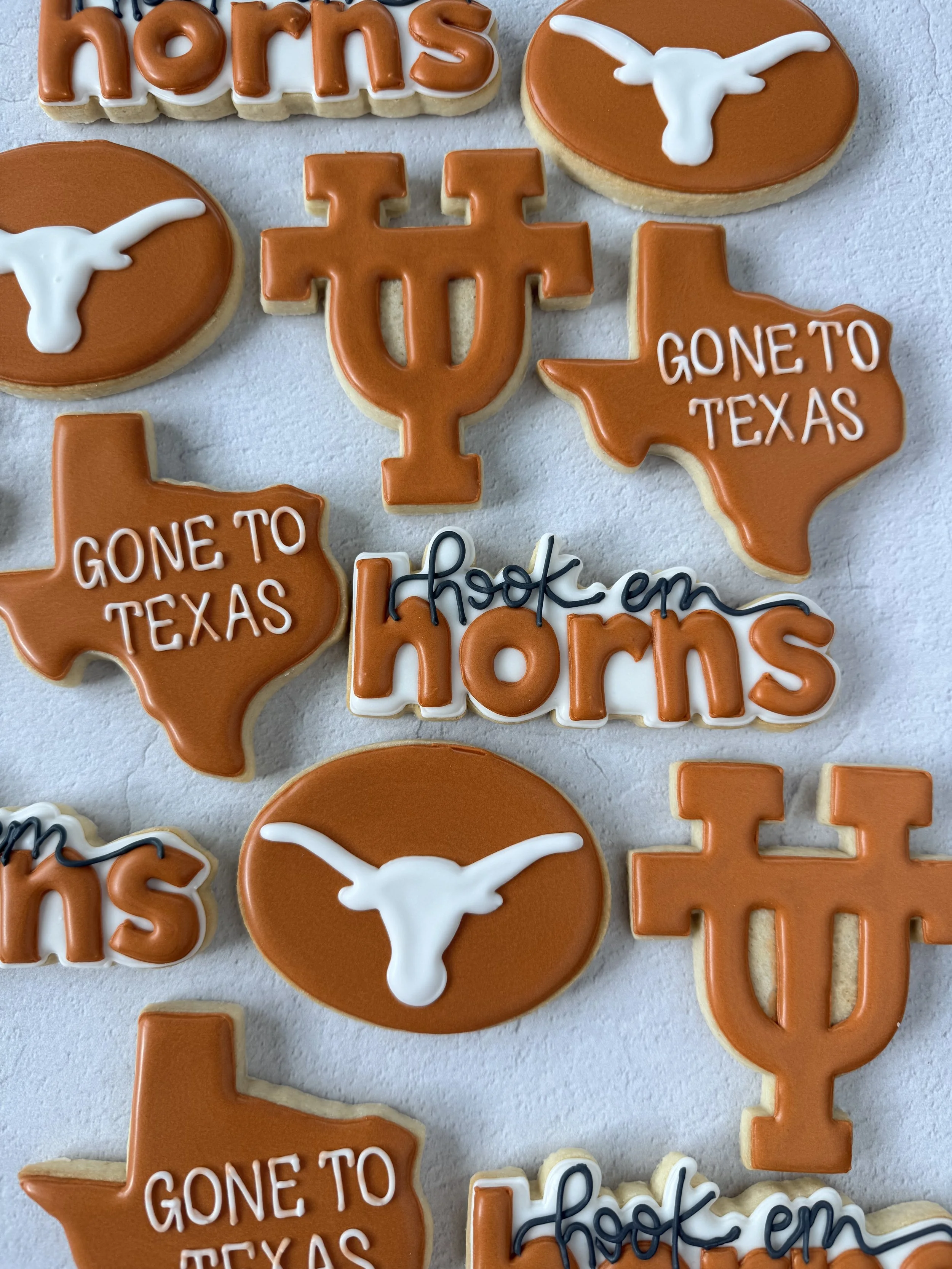 Sugar cookies decorated with orange, white, and black icing. Some cookies have the Texas state shape with 'Gone to Texas' written on them, while others feature the University of Texas logo and the UT Longhorn steer head.