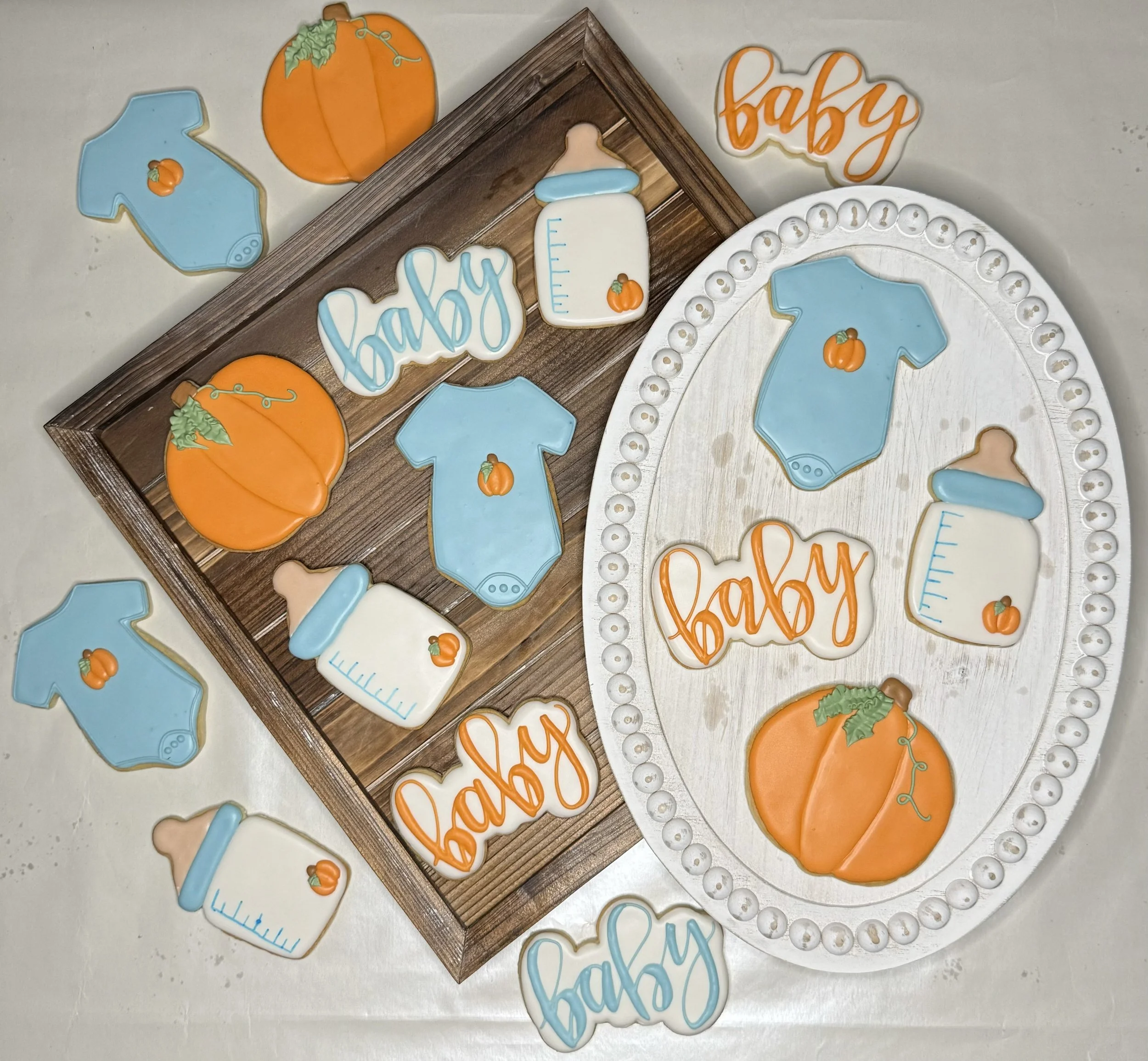 Decorative cookies for celebrating a baby, including ones shaped like a onesie, a baby bottle, a pumpkin, and words like 'baby' and 'welcome'.