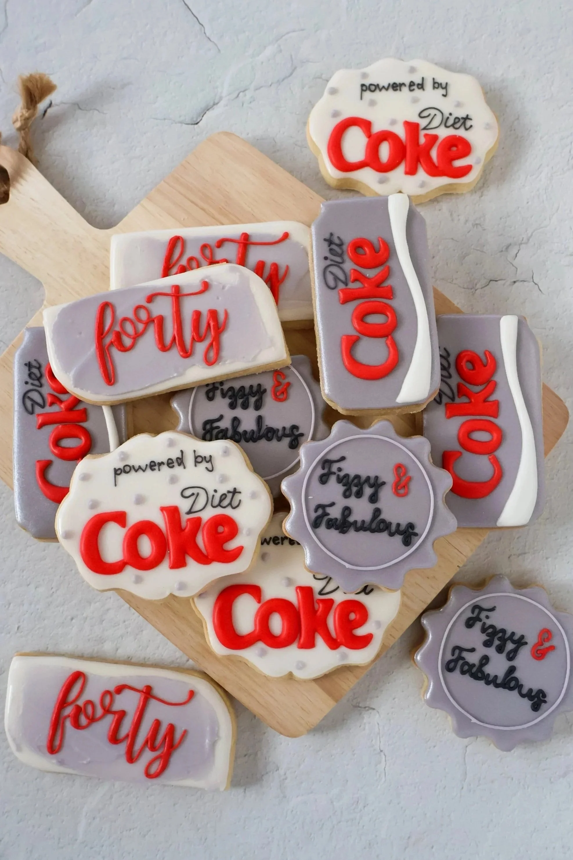 Decorative cookies in the shape of Coke bottles and signs. The cookies have white, red, and gray icing with various messages, including "powered by Diet Coke" and "fetty" written on them.