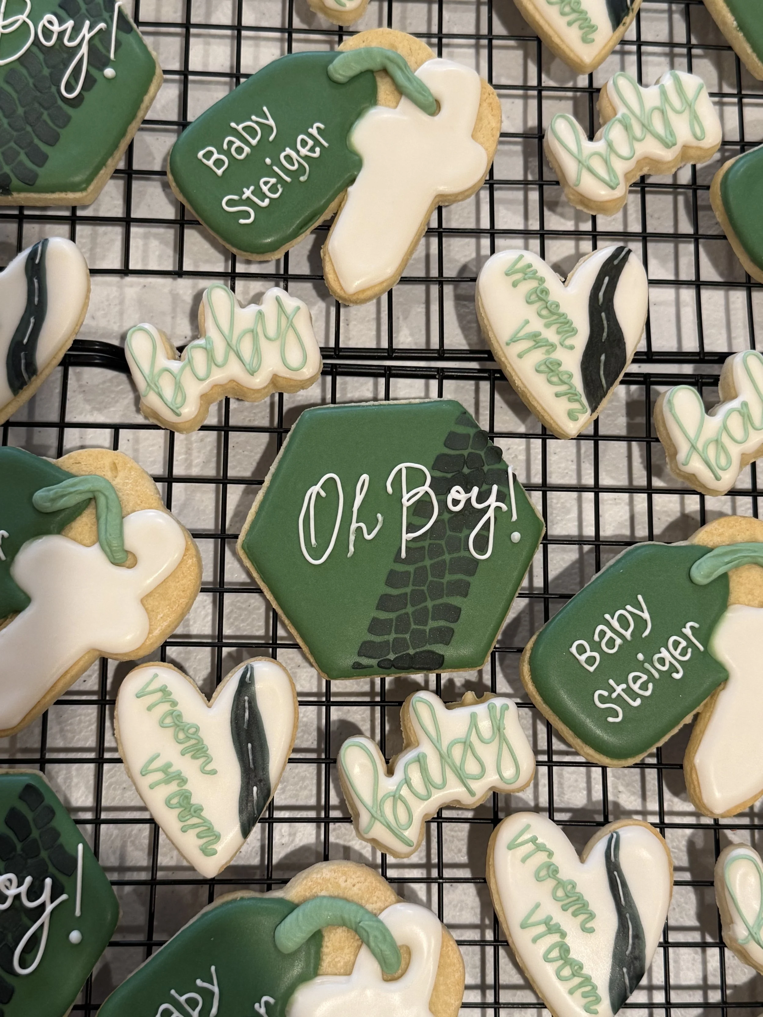 Decorated cookies with baby boy theme, featuring green and white icing, some shaped like baby bottles and hearts, with messages like "Baby Steiger" and "you're awesome".