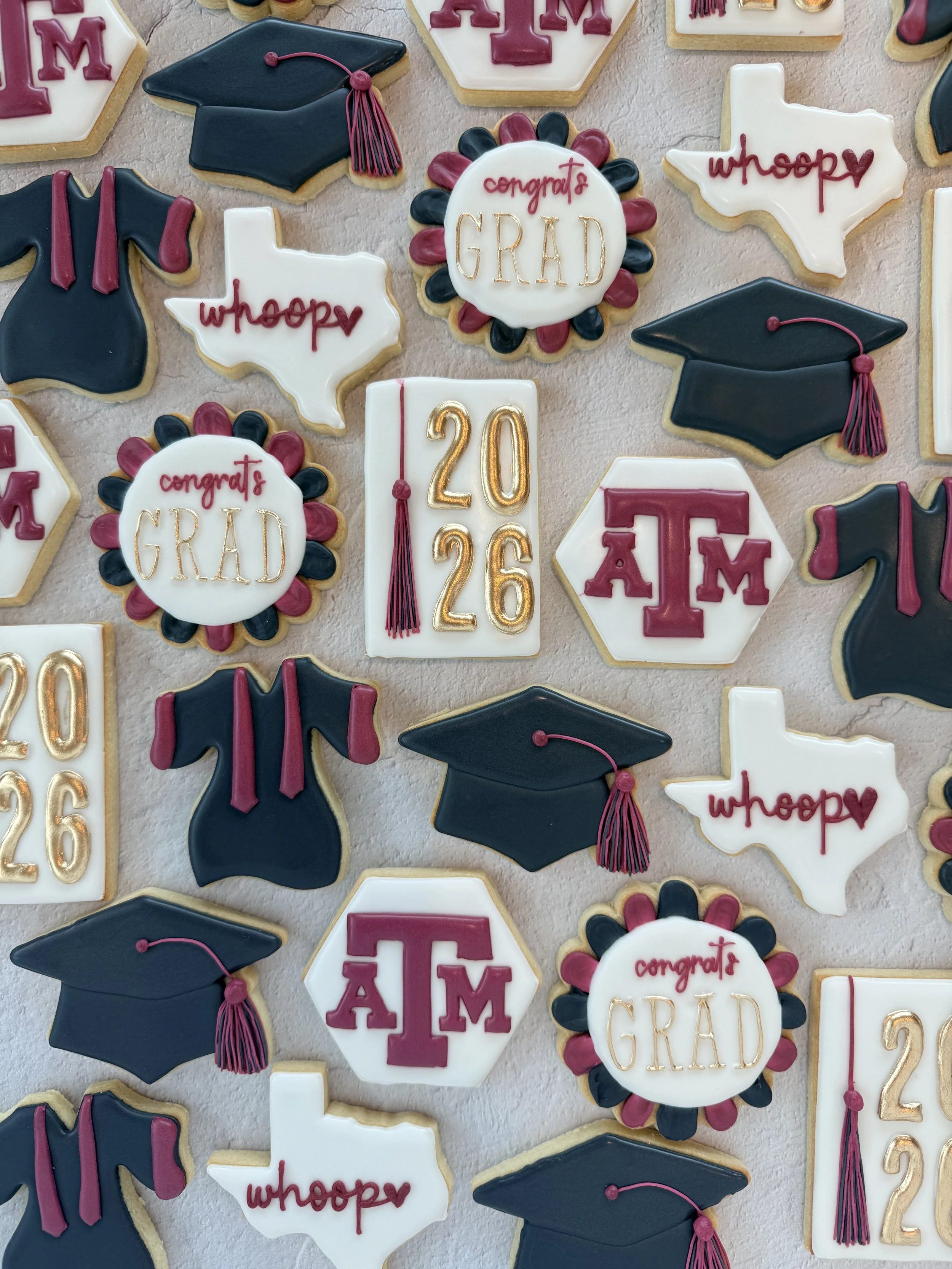 Array of decorated cookies celebrating graduation, including graduation caps, Texas-shaped cookies with 'whoop' written, and cookies with 'congrats grad' and '2026'.