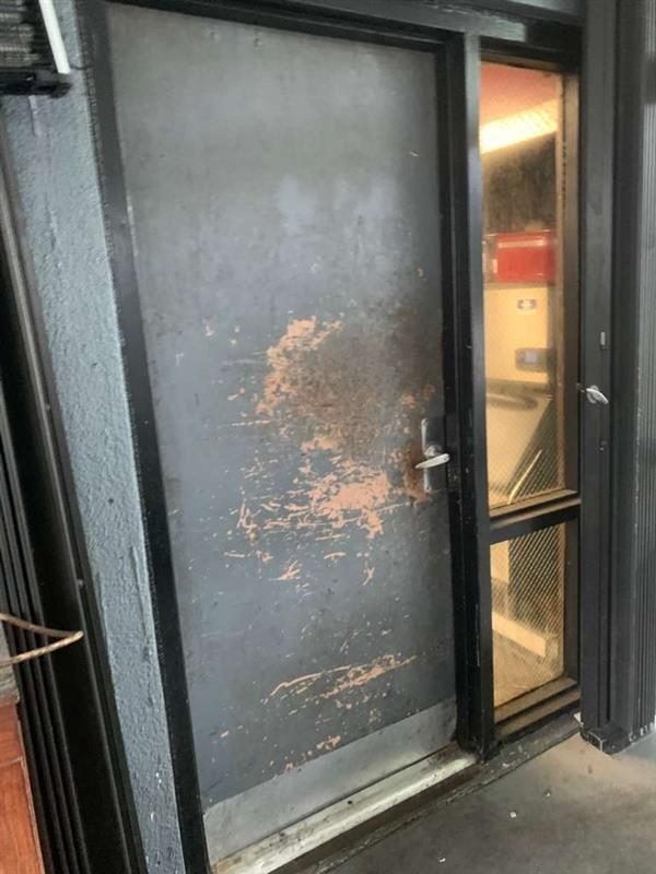 A black metal door with peeling paint and a silver handle, next to a black-framed window with a metal grid, in an industrial or commercial setting.