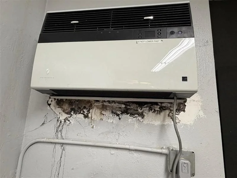 Wall-mounted air conditioning unit with mold and water damage on the wall below it.