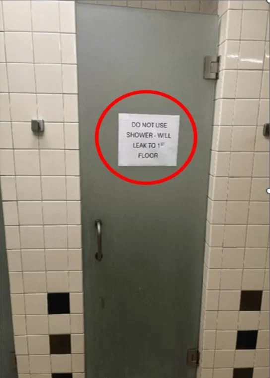Bathroom stall door with a warning sign that says, 'Do not use shower - will leak to 1st floor'.