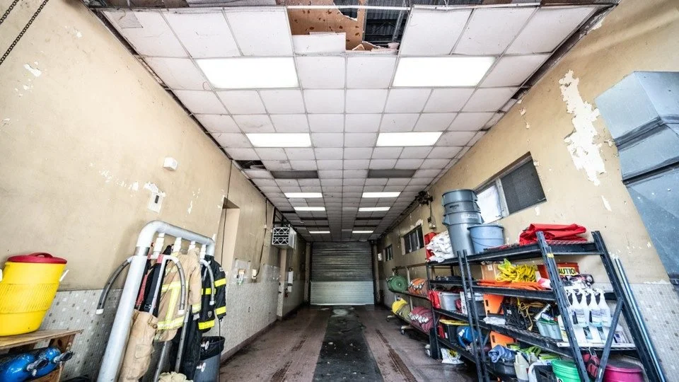 Interior of a damaged garage or storage area with a damaged ceiling, some fire safety gear, and shelves with supplies.