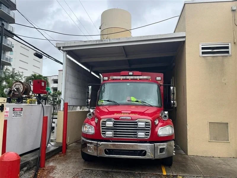 A red fire truck parked in a garage under a building with water hoses and equipment nearby.