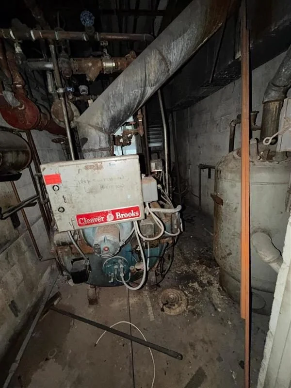 A basement with exposed pipes and a boiler labeled "Clever Brooks."