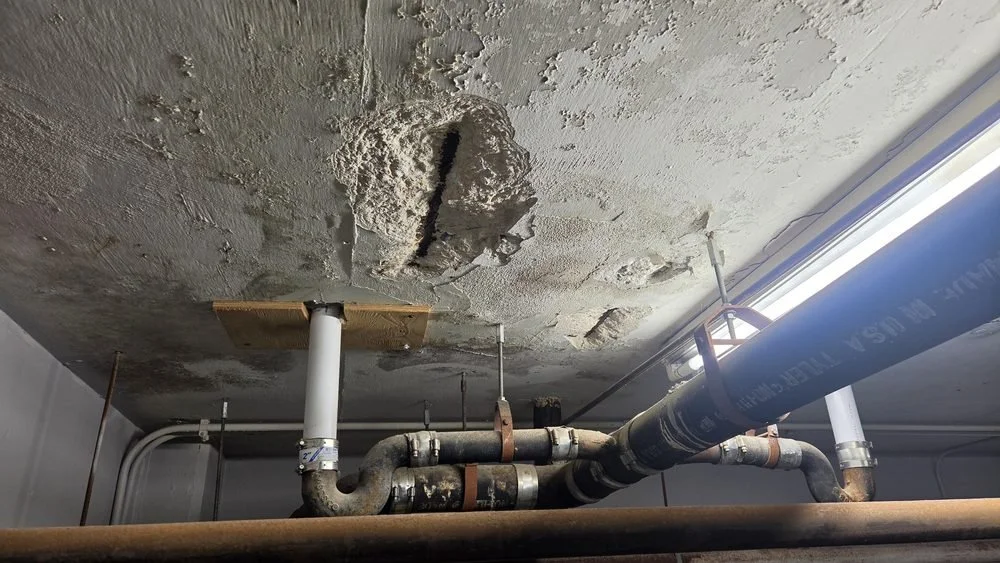 Ceiling with a large hole and exposed pipes in a building.