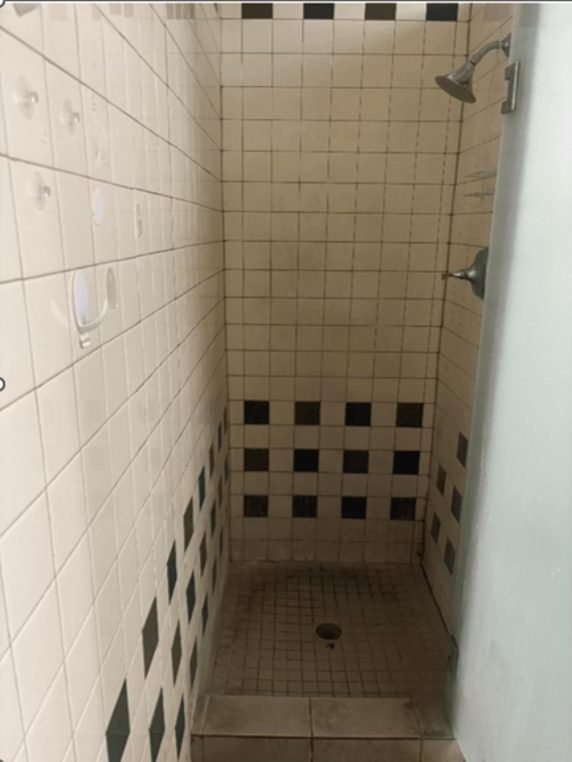 Empty shower with tiled walls and floor, featuring a showerhead on the right wall and a drain on the tiled floor.