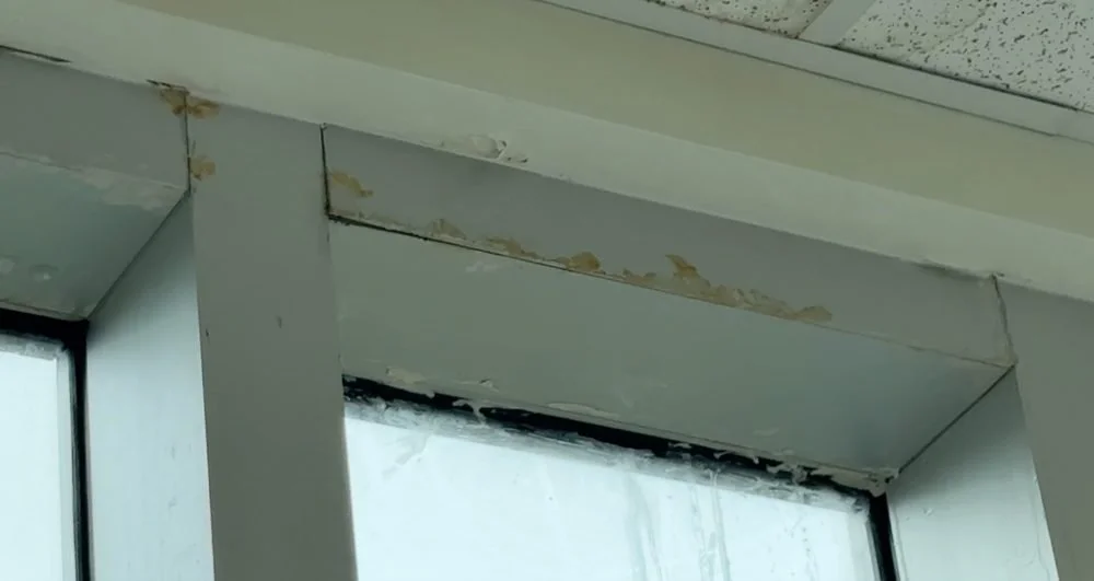 Close-up of a window frame with peeling paint and water stains.