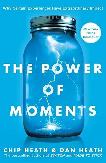 A book cover titled 'The Power of Moments' by Chip Heath and Dan Heath. The cover features a jar with lightning inside, set against a bright blue background.