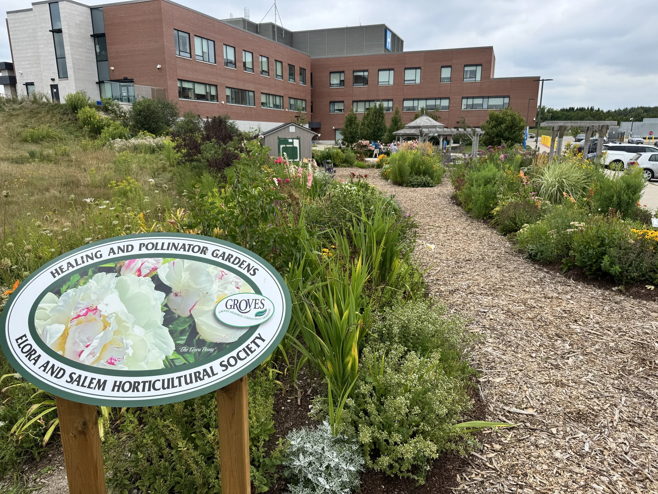 Photo of the Elora & Salem Healing & Pollinator Garden Sign in front of gardens and a pathway