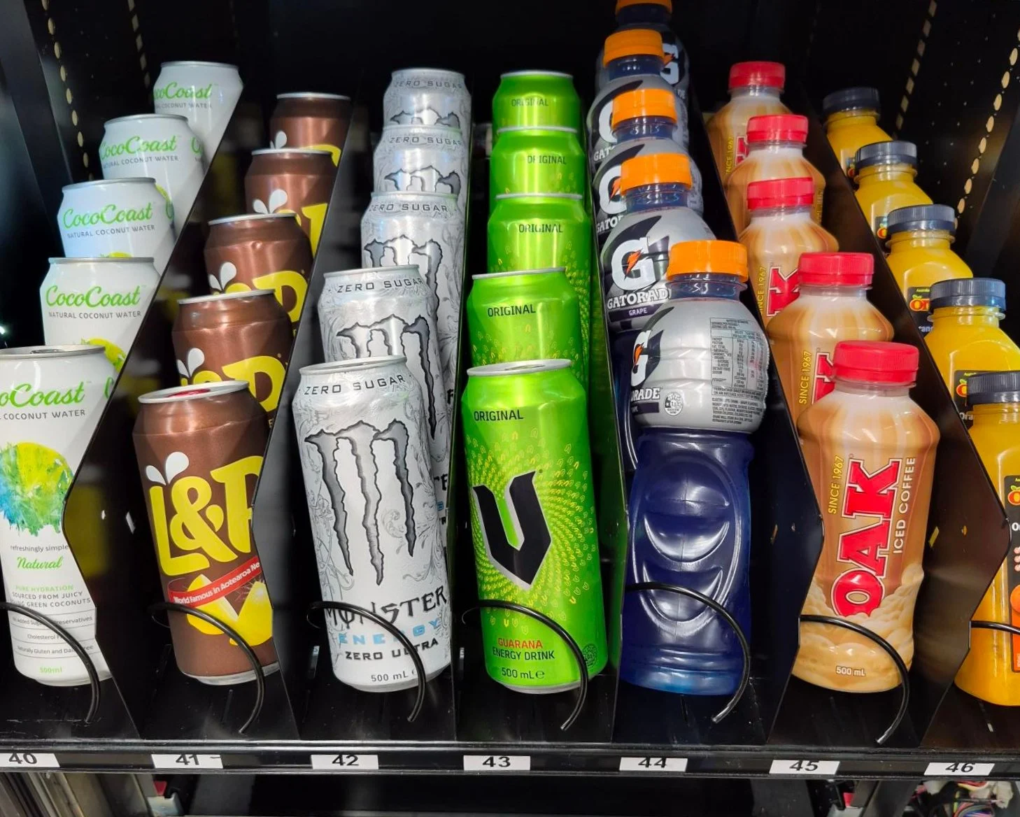 An open vending machine with drinks: Coconut water, L&P, Monster White, V, Gatorade, Oak and Orange Juice