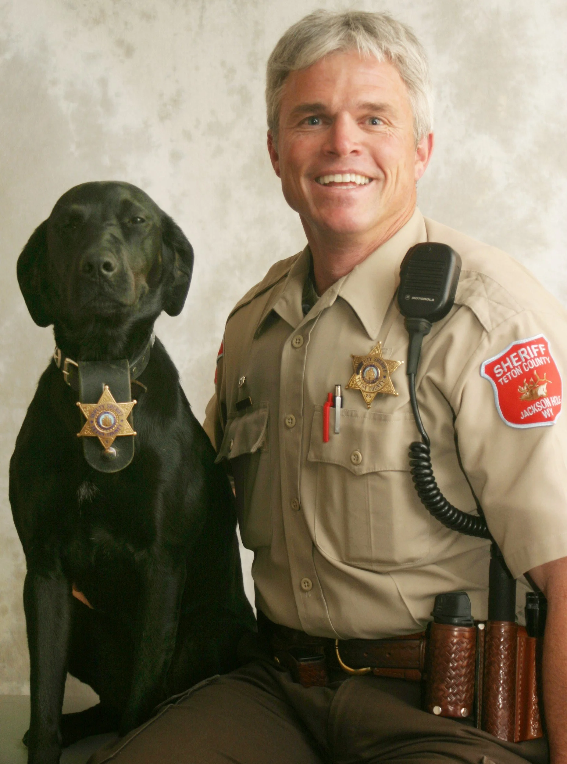 Dave Hodges and his dog, Pepper, both wearing sheriff badges, against a plain background.