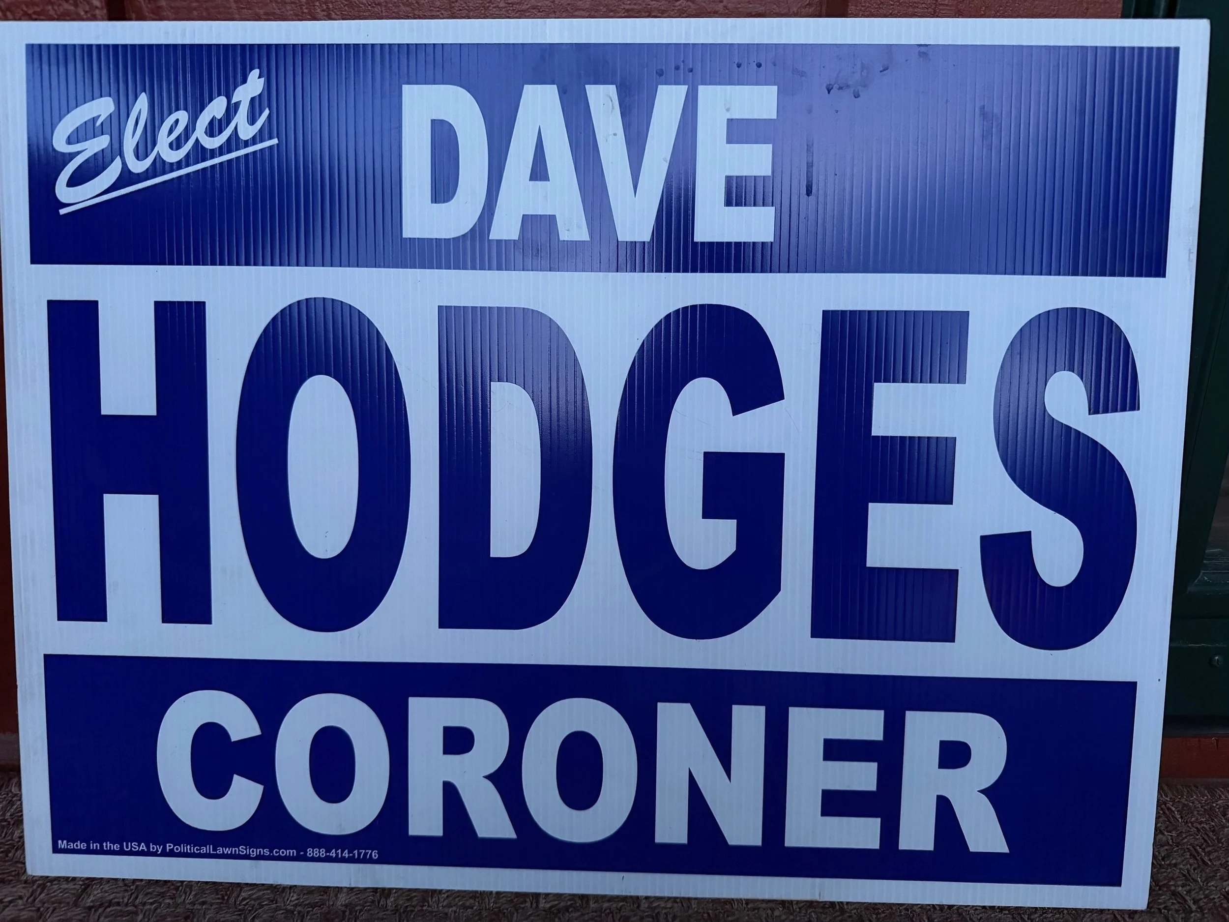 Dave Hodges' political campaign sign with the text 'Elect DAVE' in white on a blue background, and the phrase '100% CORONER' below in large white letters.