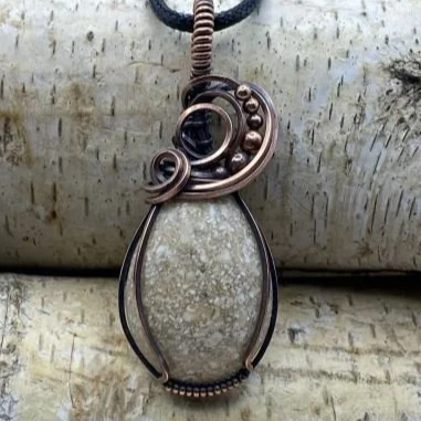 A pendant necklace with a large stone encased in wire wrapping, featuring a spiral design and small beads on a black cord.