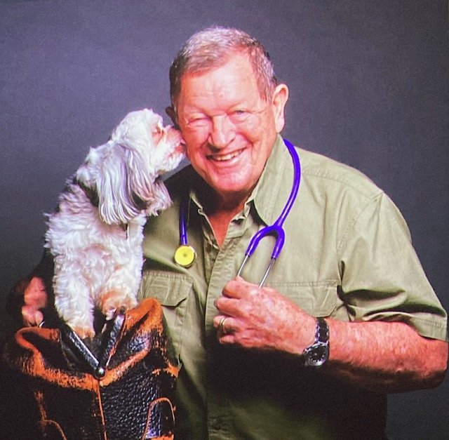 Elderly veterinarian being licked by a fuzzy white puppy he's holding
