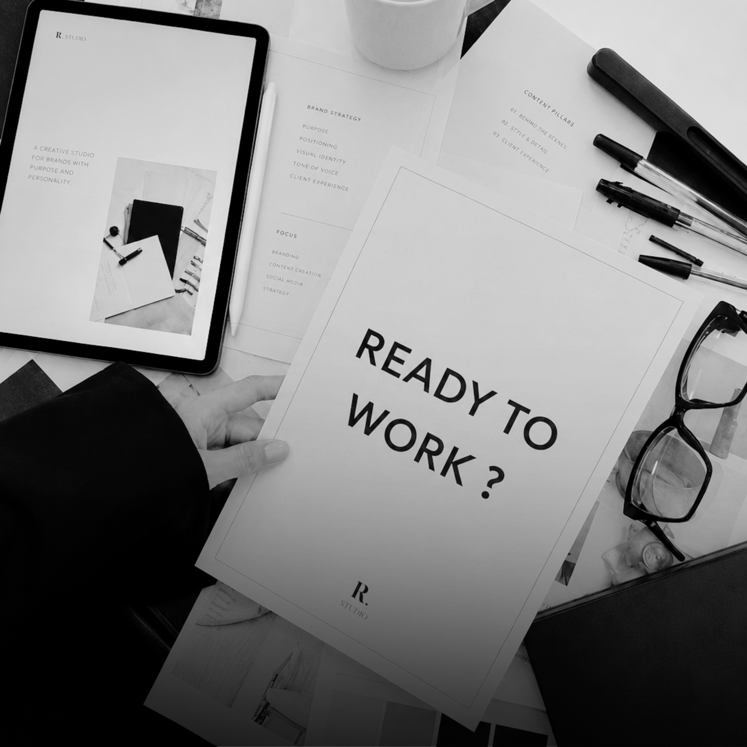 A flat lay of office supplies and documents on a desk, including a tablet, markers, and printed papers with text, in black and white.