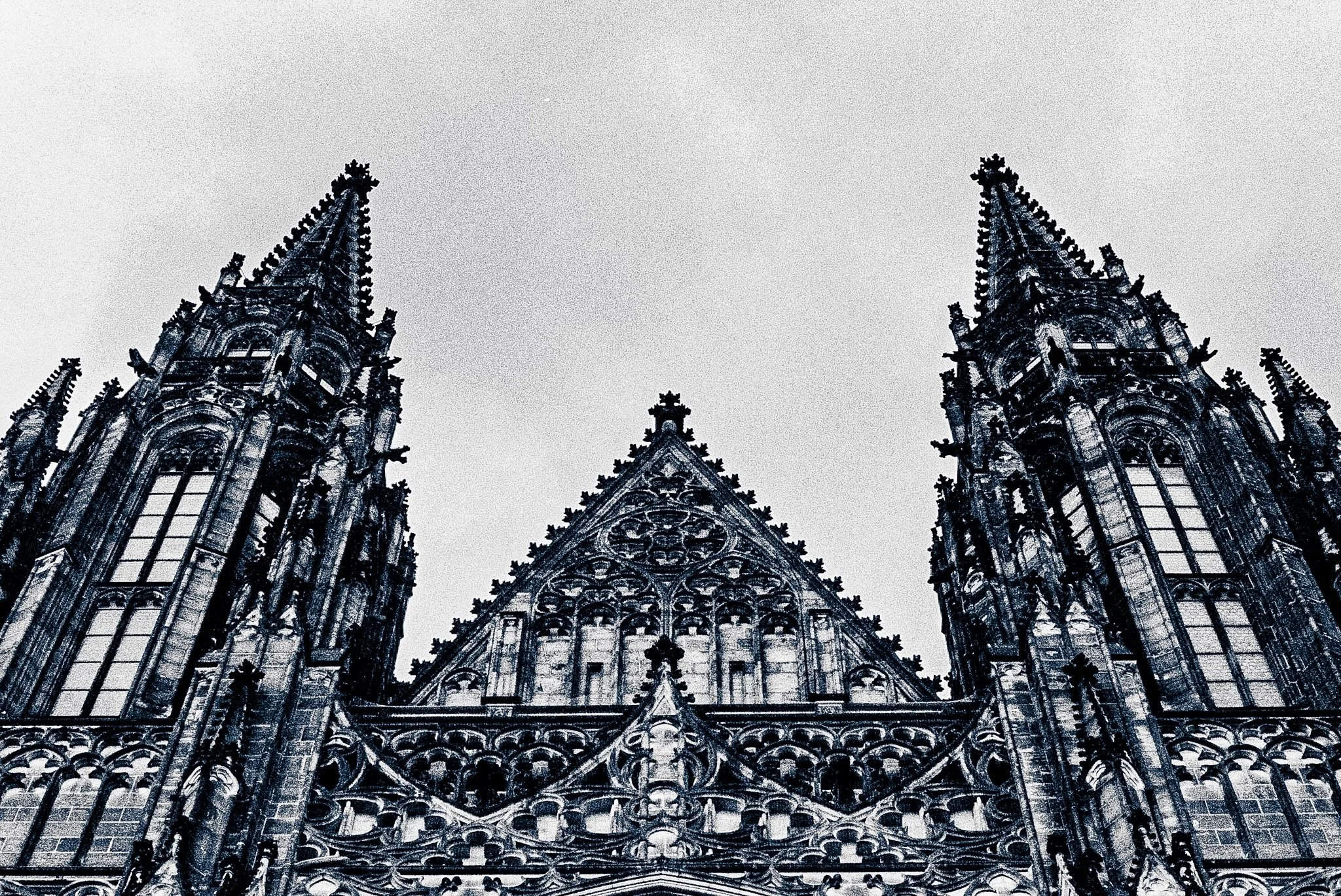 Low-angle view of a Gothic cathedral facade with spires and intricate stone carvings against a cloudy sky.