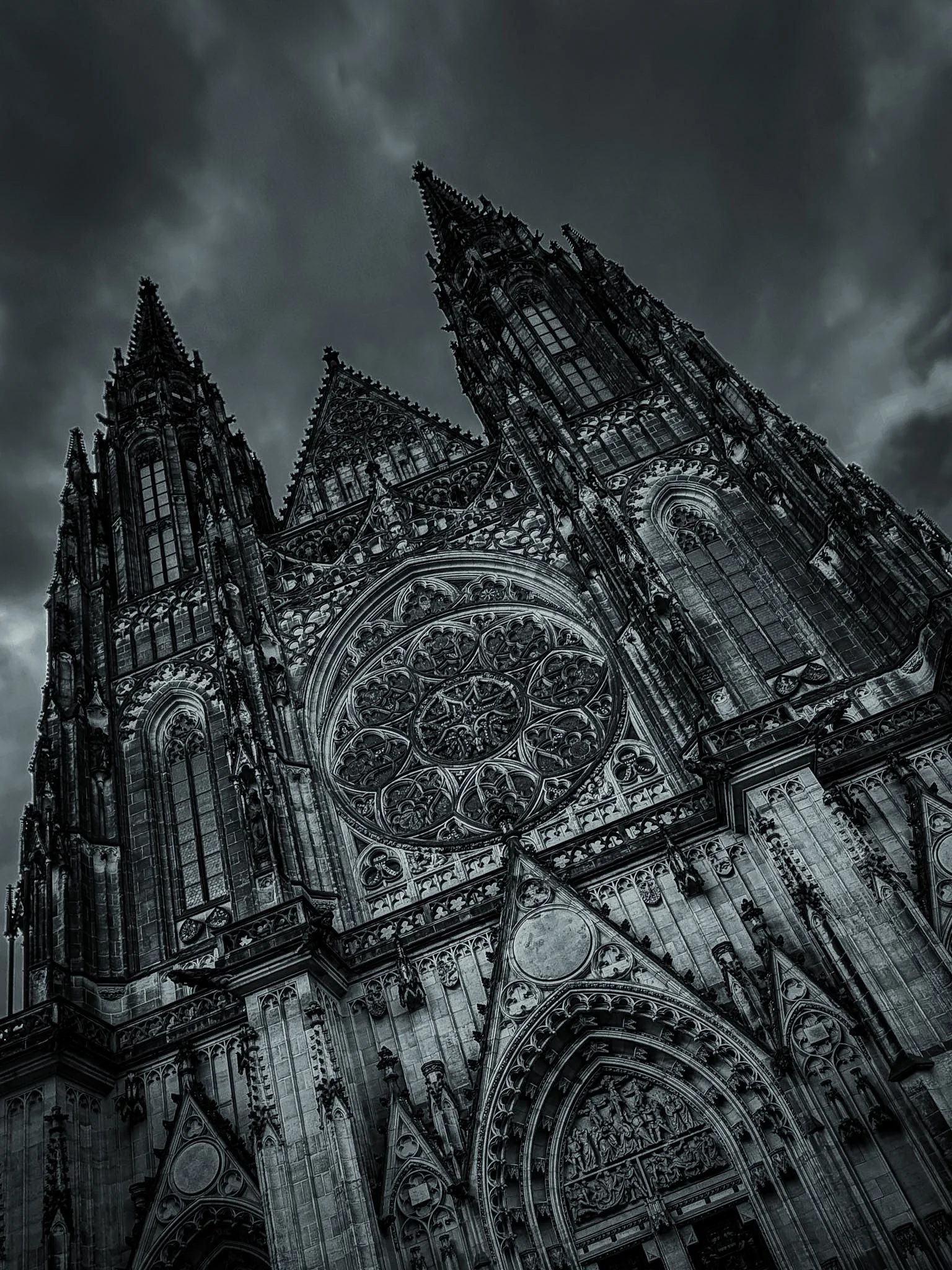 A Gothic cathedral with intricate stone carvings, pointed arches, and tall spires, viewed from a low angle against a cloudy, dark sky.
