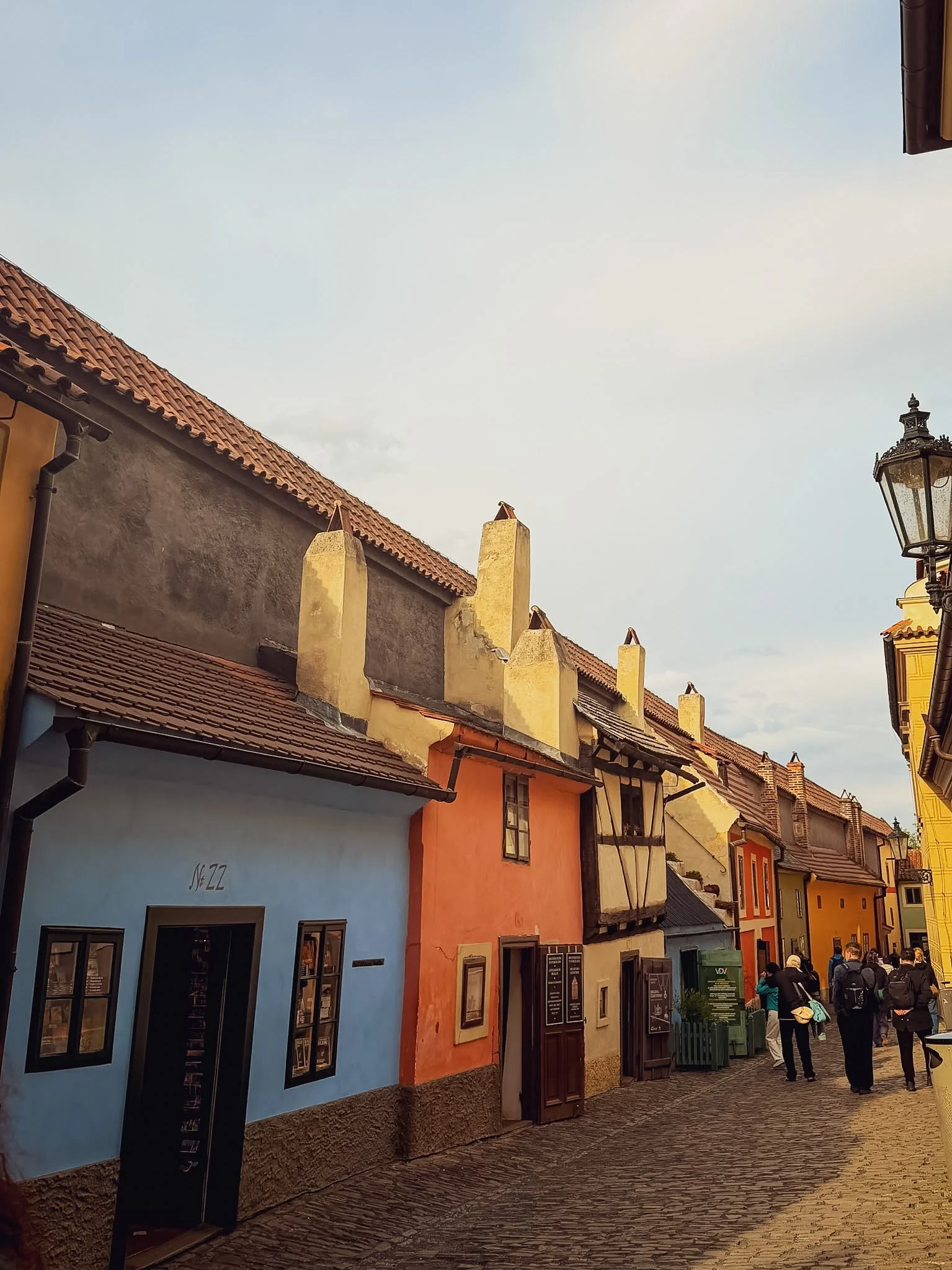 Colorful row houses on a cobblestone street, with people walking and a street lamp on the right.