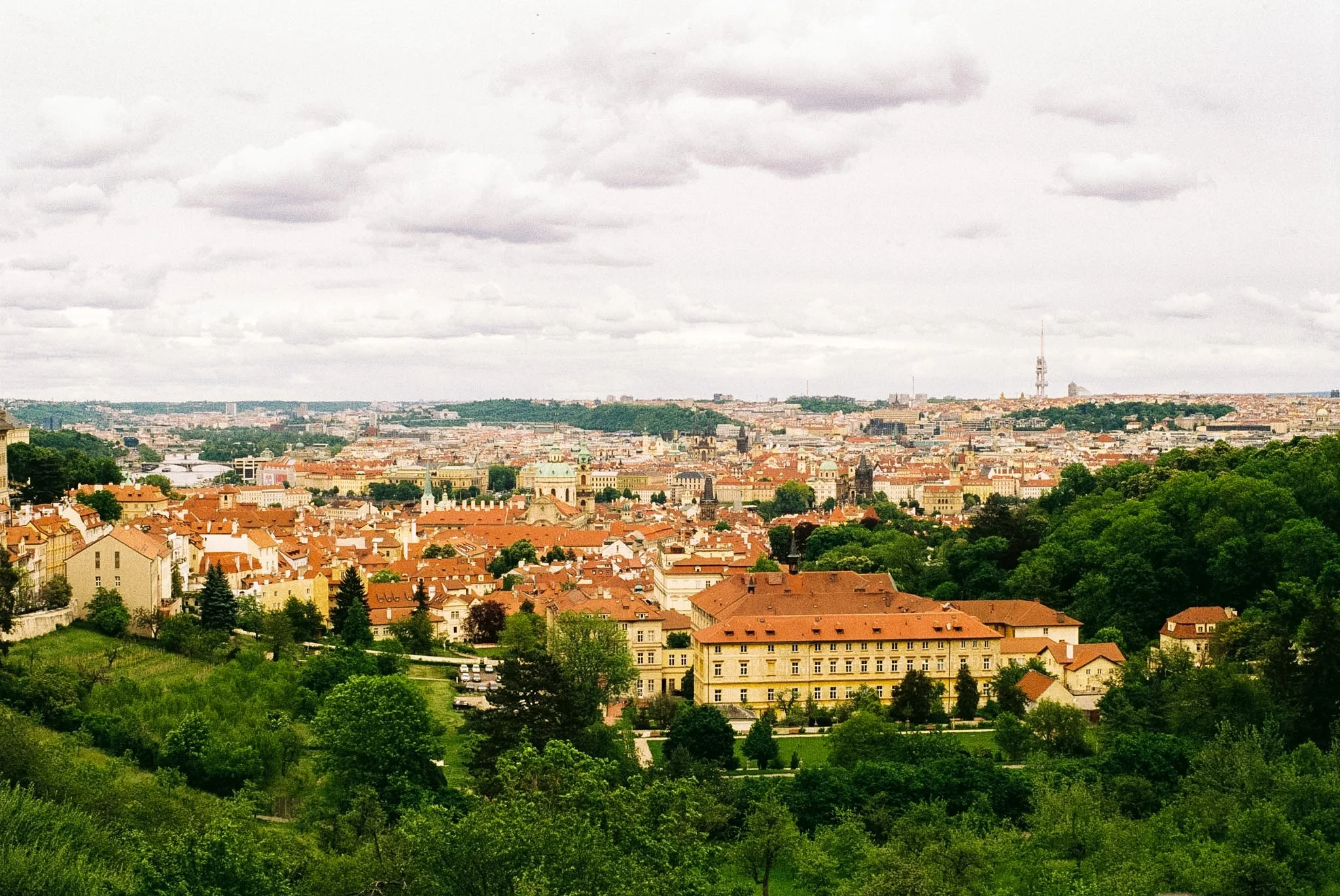 A panoramic cityscape featuring historic and modern buildings, with a tower in the distance, under a cloudy sky.