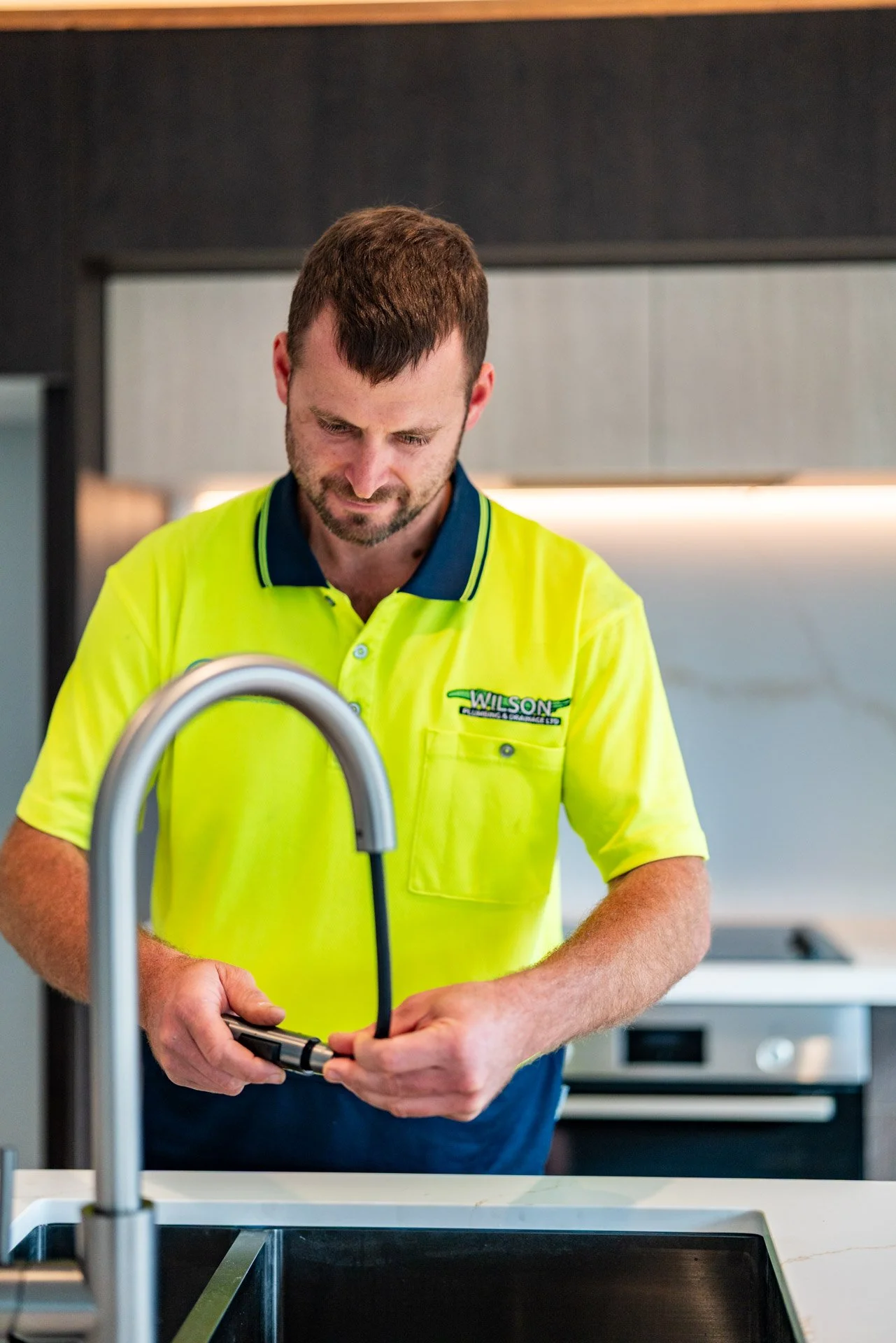 Man in yellow work shirt filling sink with water in modern kitchen.