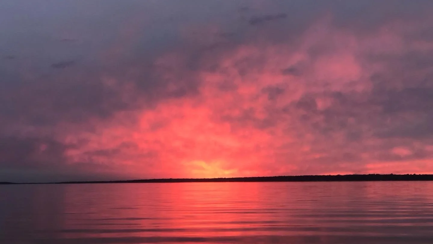 Sunset over a calm body of water with pink and purple clouds in the sky.