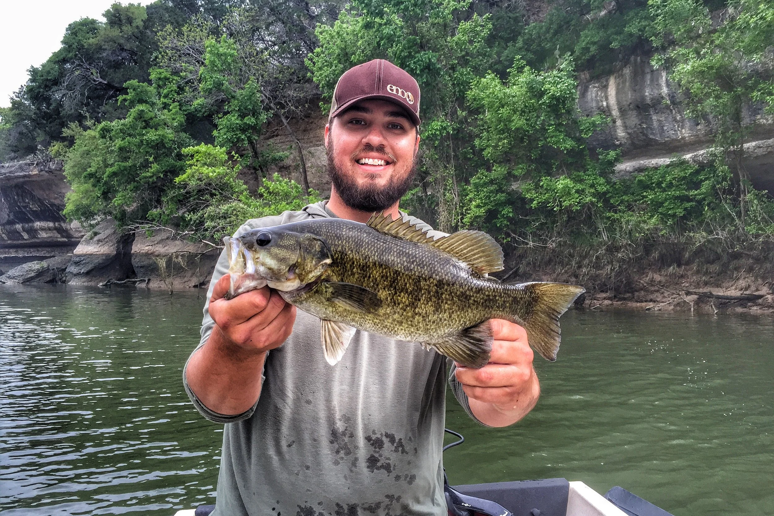 A man holding a large fish with water and trees in the background.