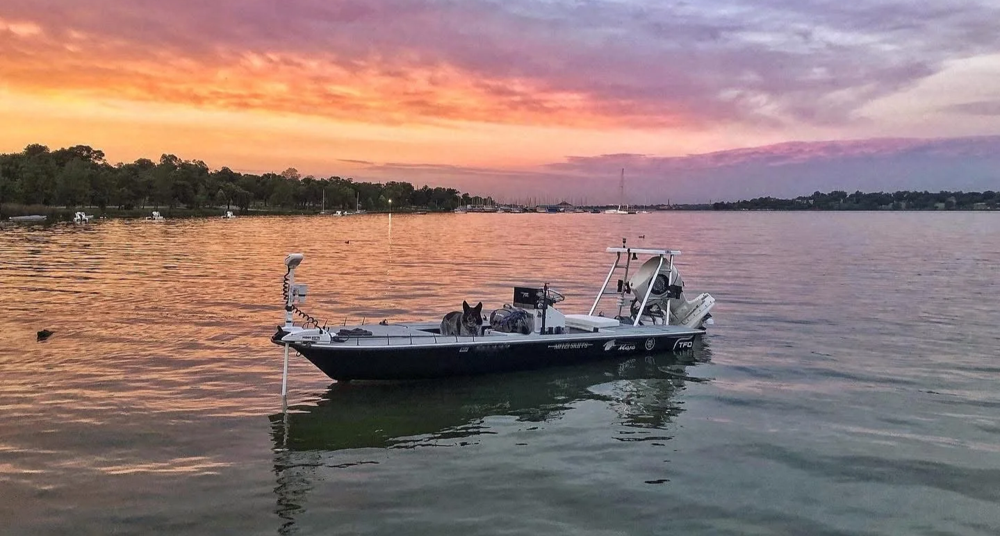 A boat floating on water during sunset with a dog on board and a scenic sky in background.