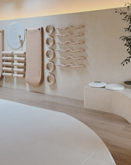 Minimalist interior with wall-mounted circular objects, curved handrails, and a seating area. The space features light-colored walls and wooden accents.