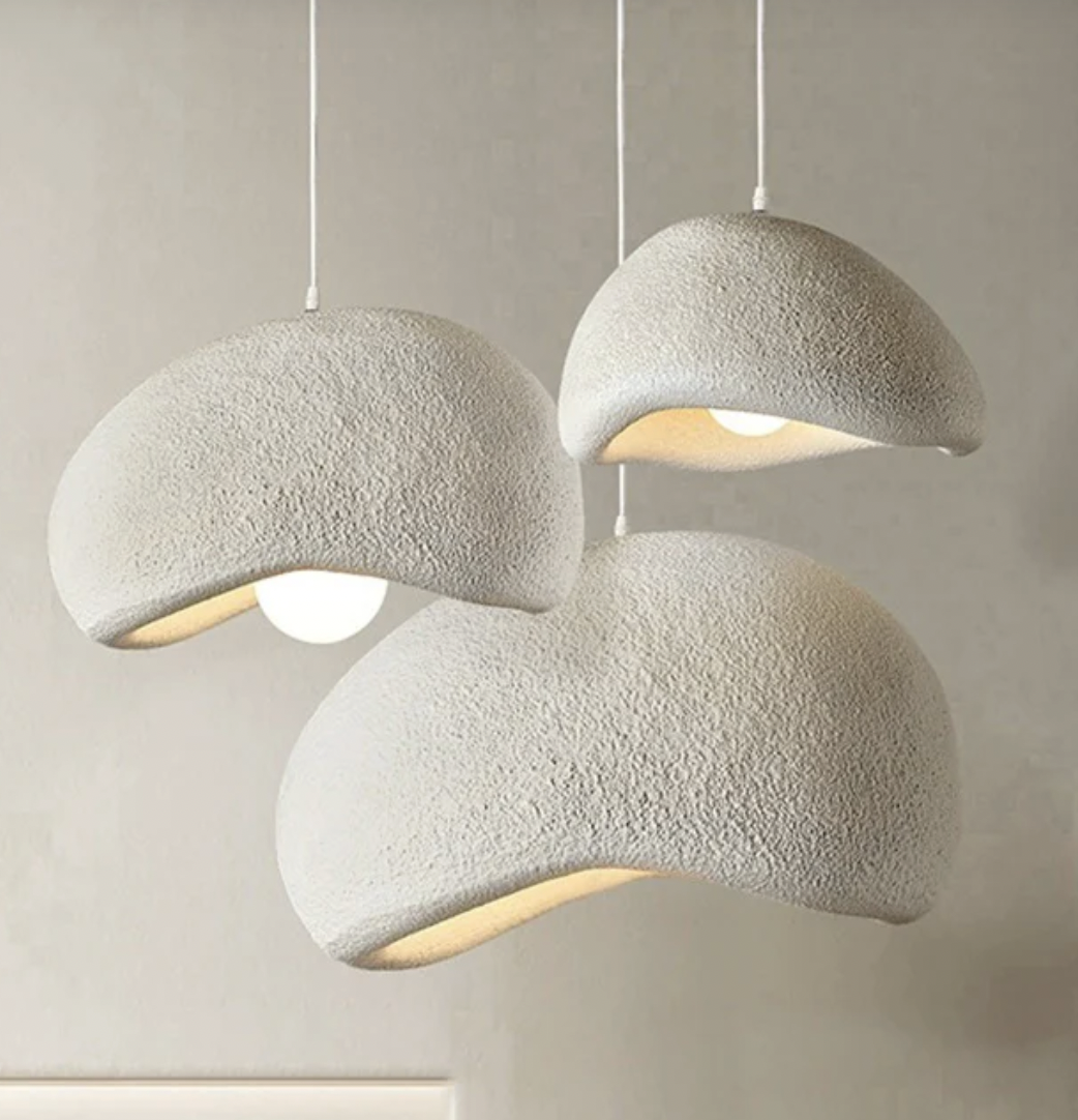 Three hanging modern pendant lights with textured, beige, mushroom-shaped shades and glowing bulbs against a plain background.