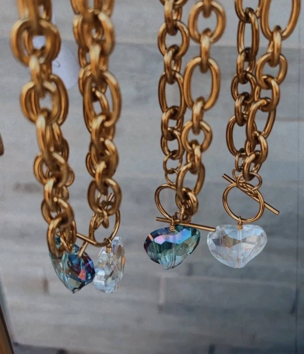 Close-up of gold-colored chain necklaces with multicolored faceted crystal pendants hanging from them.