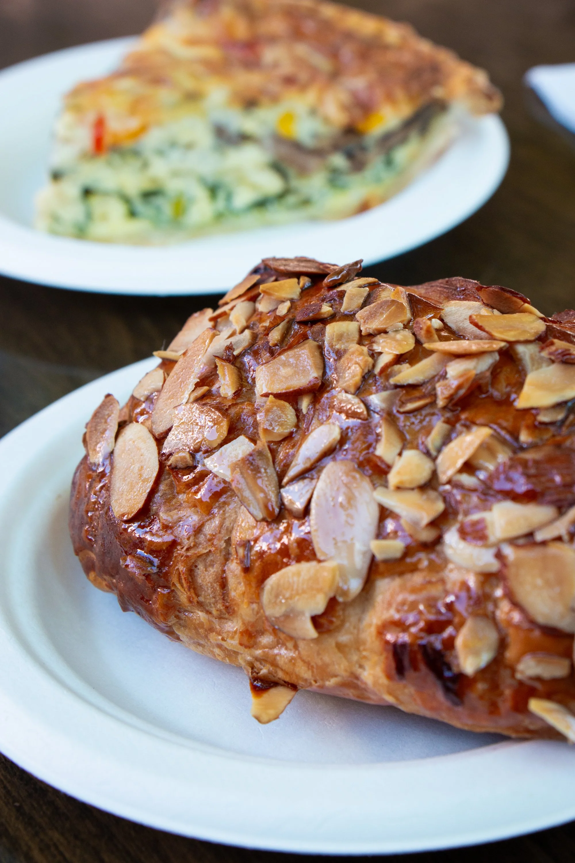 A close-up of a caramel apple topped with sliced almonds on a white plate.