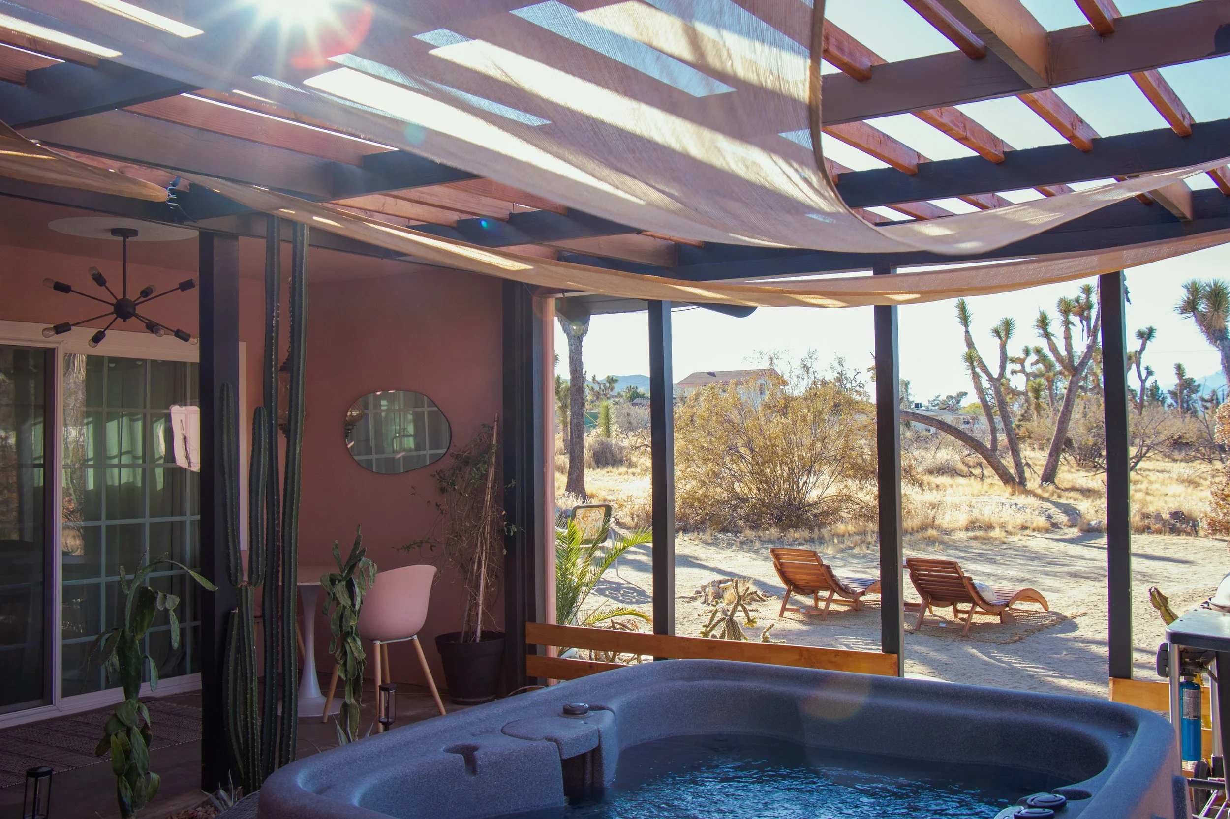 Covered patio overlooking desert landscape with cacti and trees, with outdoor lounge chairs and a hot tub in the foreground.