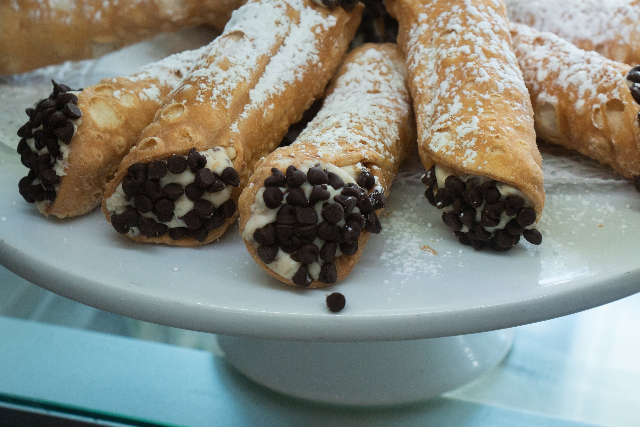 Close-up of cannoli pastries with chocolate chips and powdered sugar on a white plate.