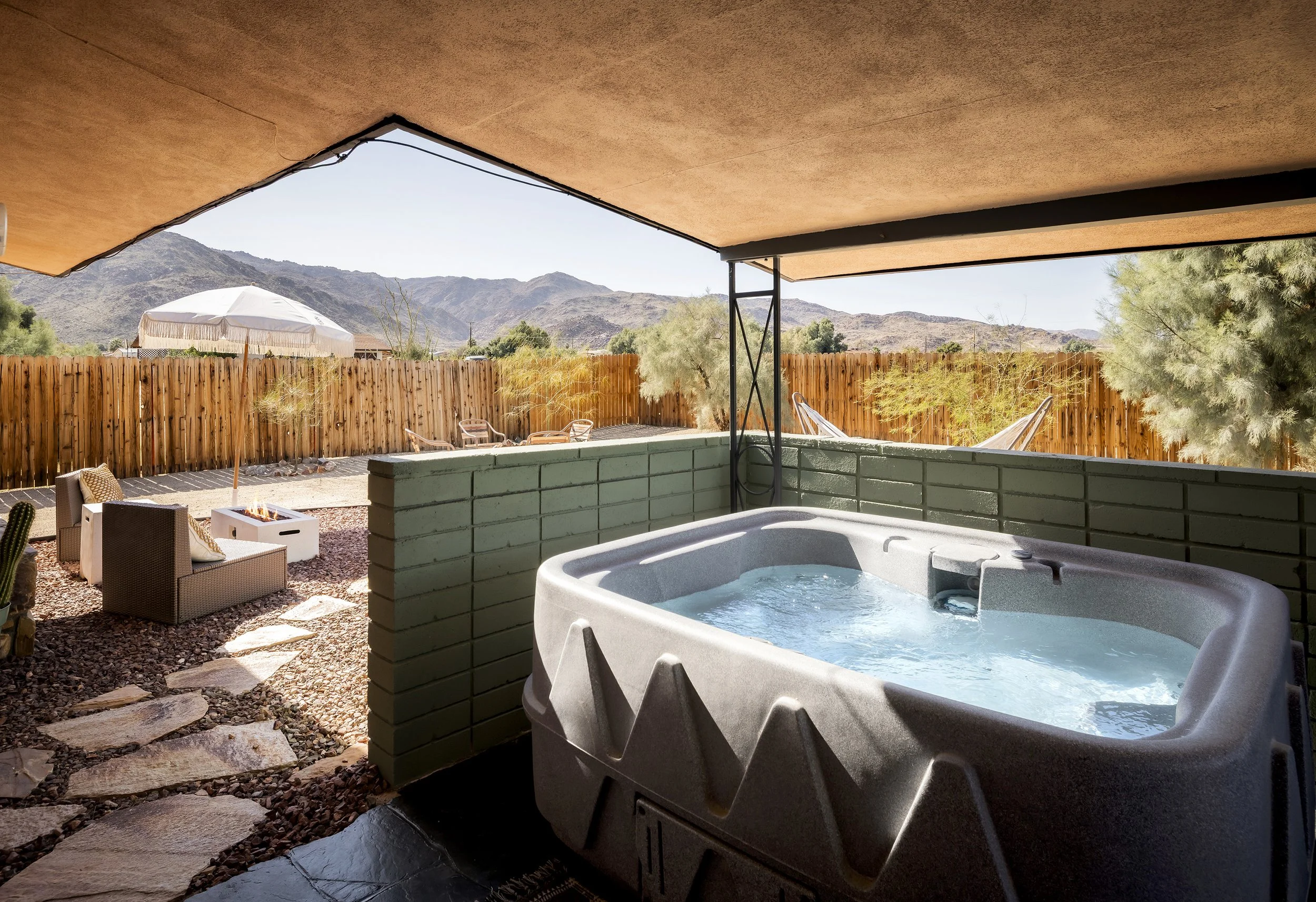 A backyard patio with a hot tub, outdoor seating, a fire pit, and a view of mountains in the distance.