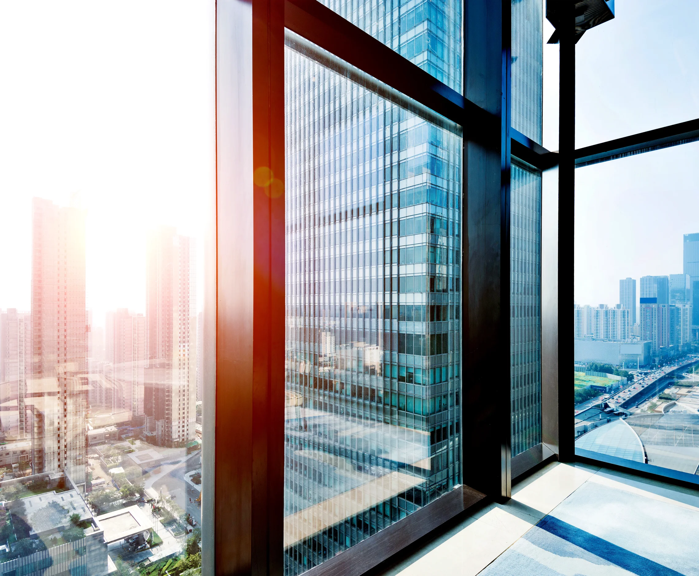 View from a high-rise building window showing modern glass and steel skyscrapers and city streets below on a sunny day.